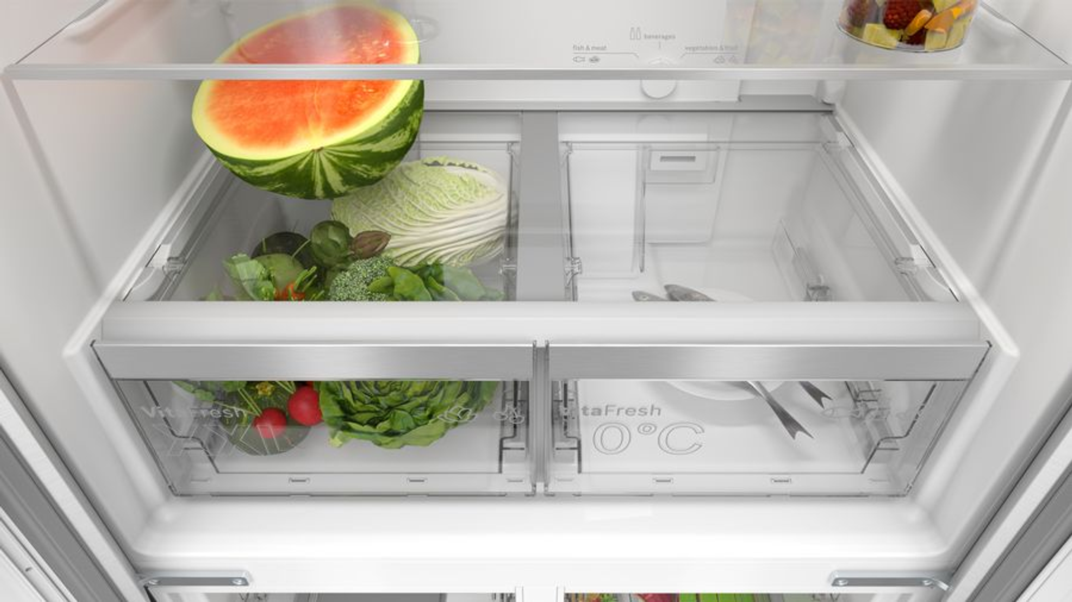 Wnętrze lodówki z szufladami zawierającymi warzywa i arbuza.