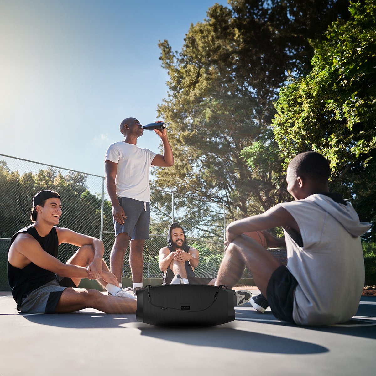 Vier mannen zitten op een tennisbaan, een drinkt water, een houdt een tas vast.