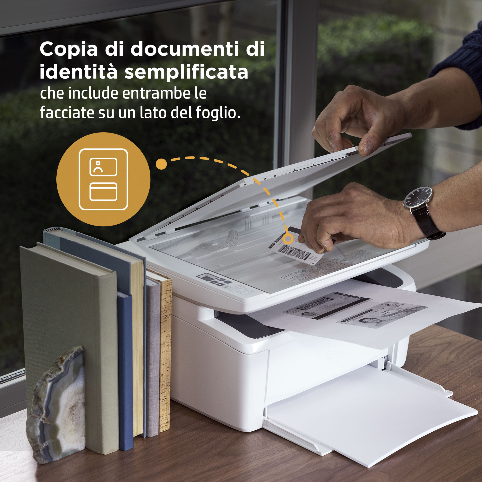 Una persona che scansiona documenti su una stampante. Libri e una pietra sono sul tavolo.