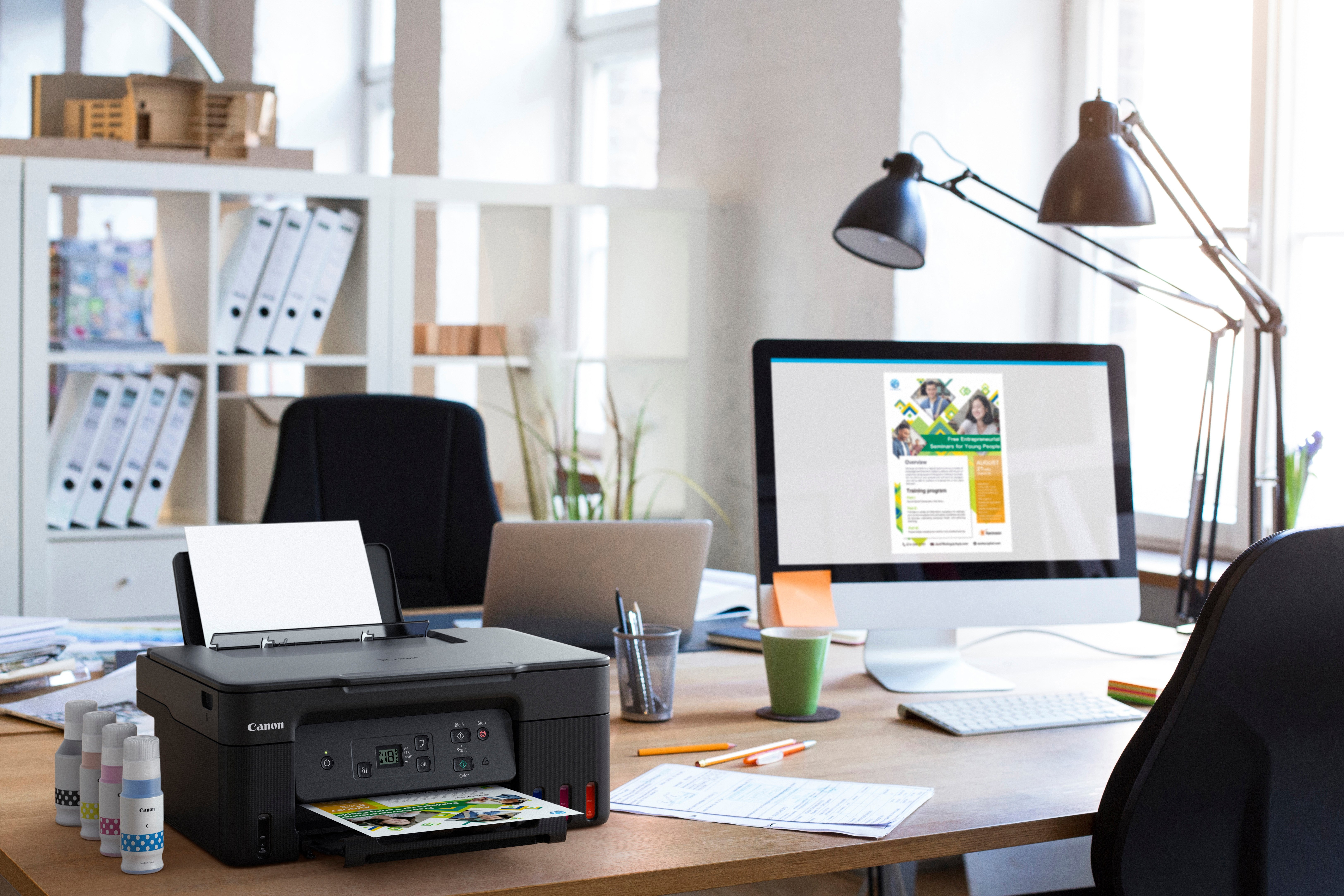 Biurko z drukarką, laptopem, monitorem i materiałami biurowymi.