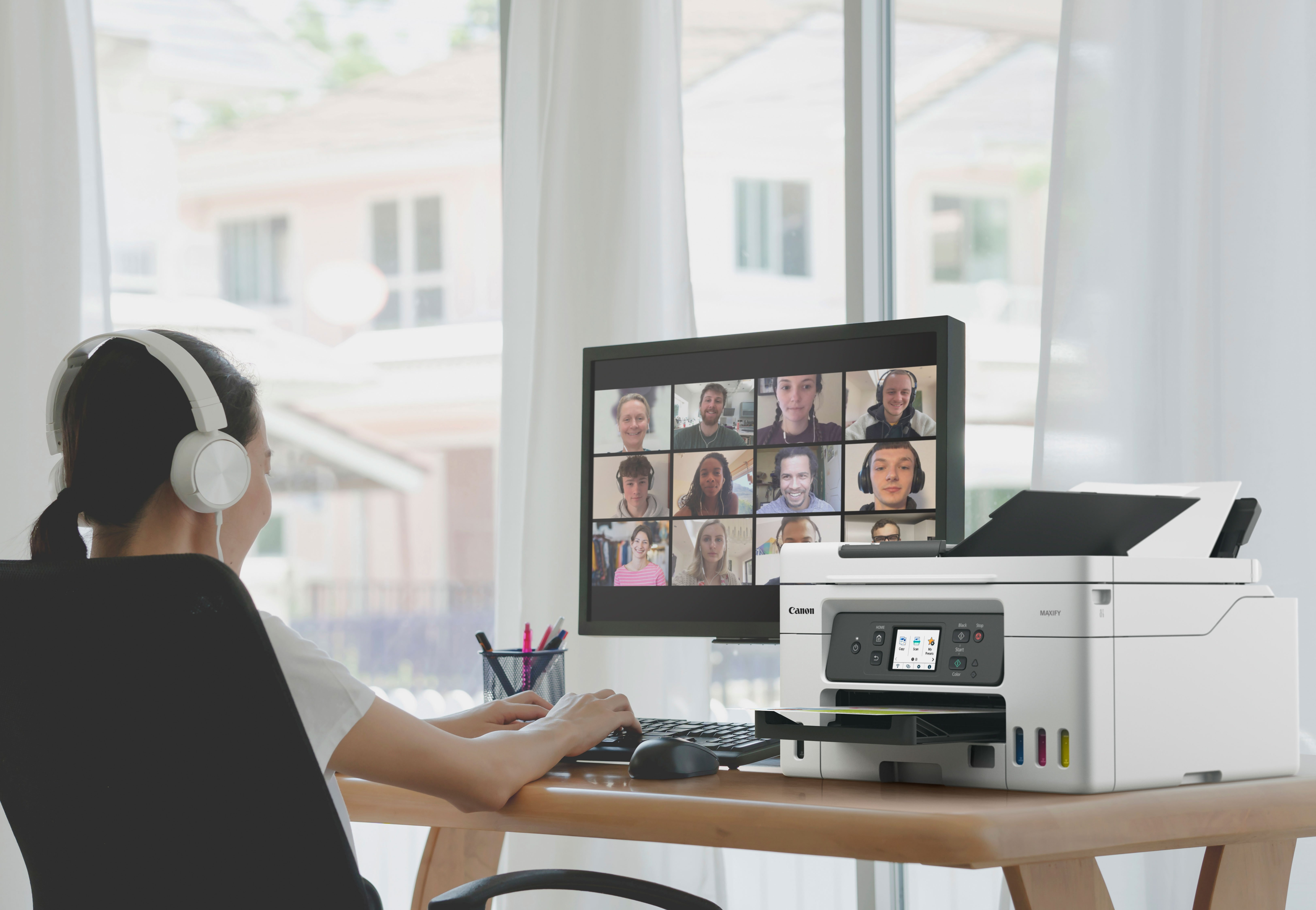 Mujer con auriculares usando una computadora para una videollamada y una impresora cerca.