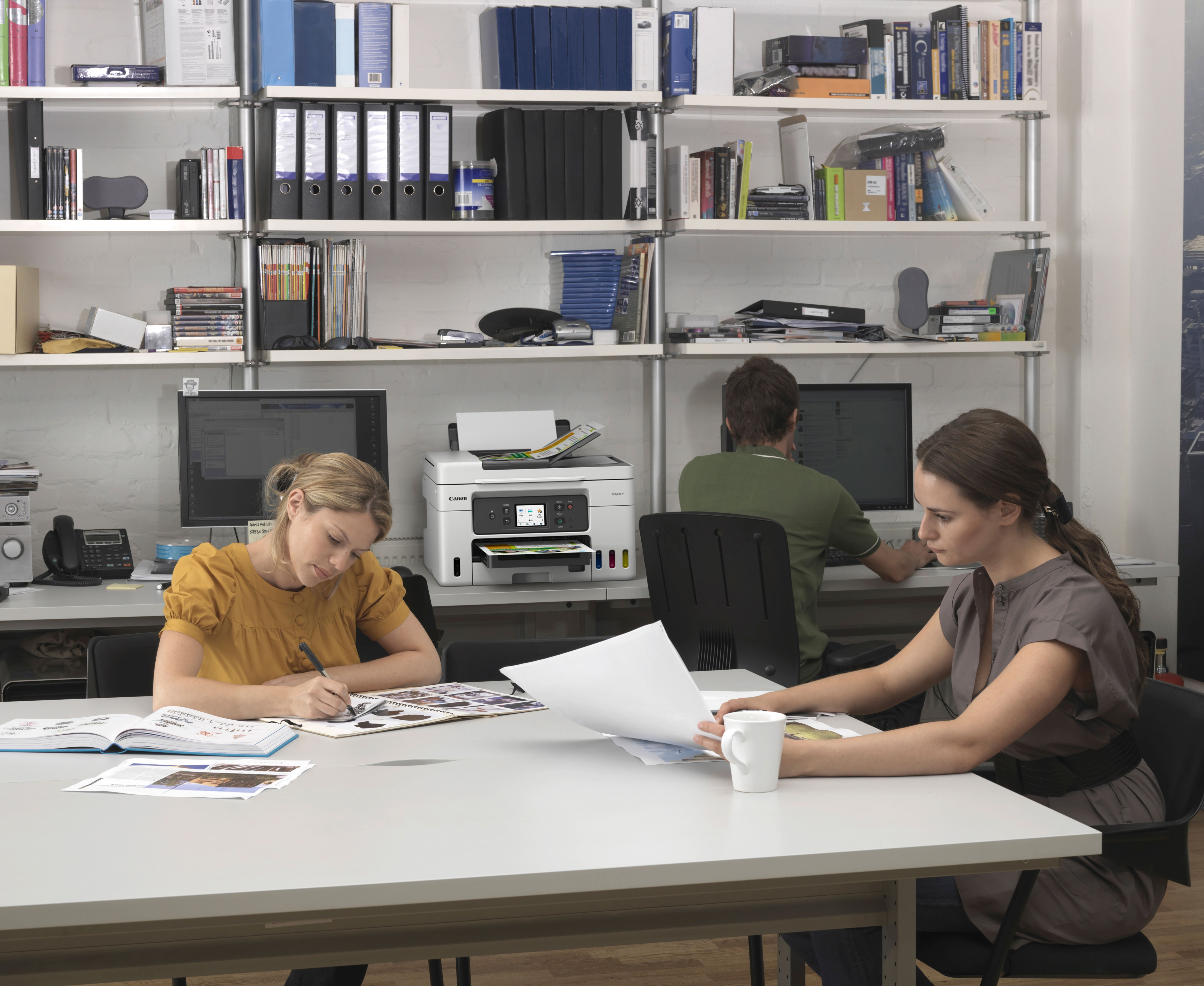 Escena de oficina con tres personas trabajando cerca de una impresora.