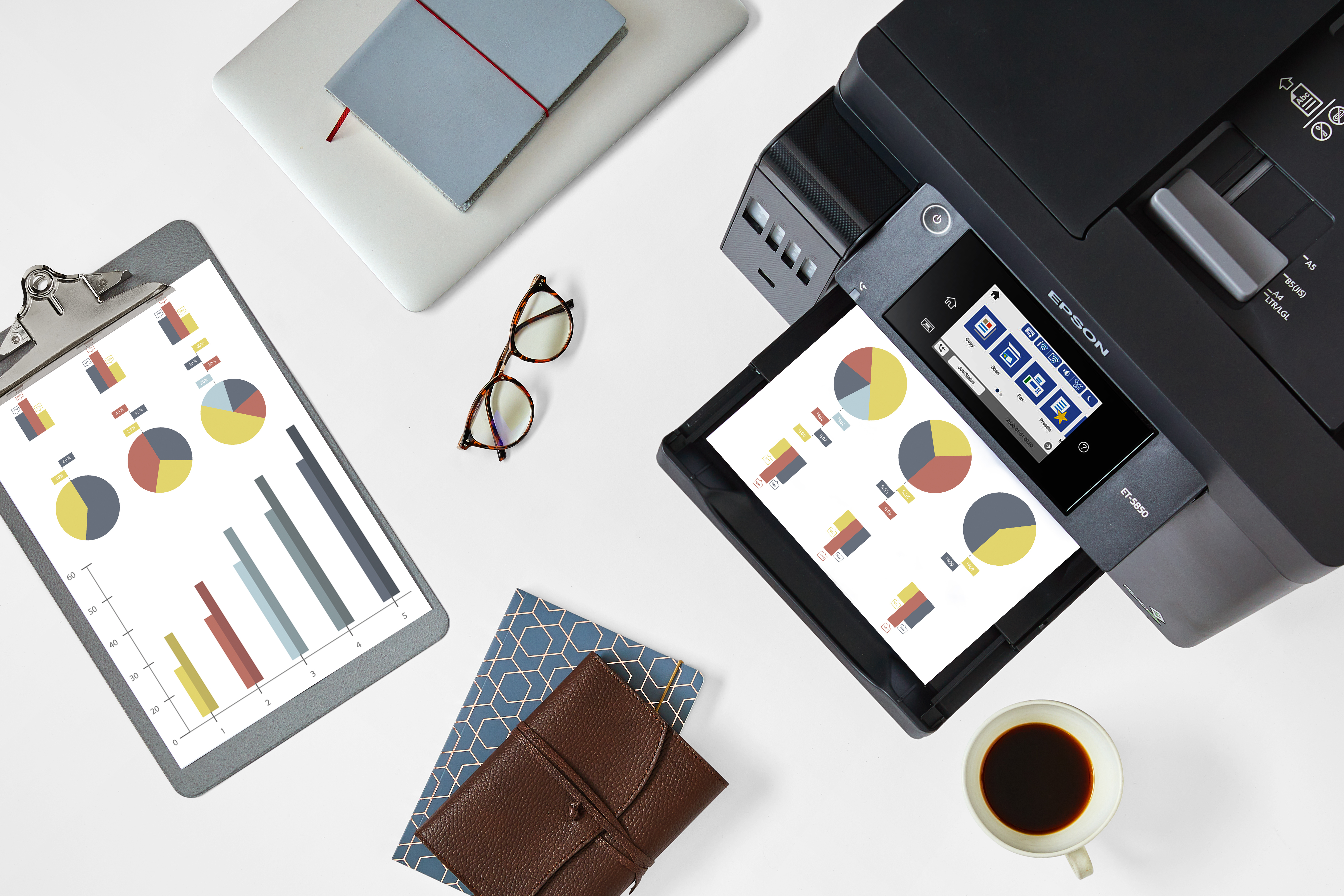 Drukarka na biurku z dokumentami, okularami i laptopem. Widoczne są wykresy kołowe i słupkowe.