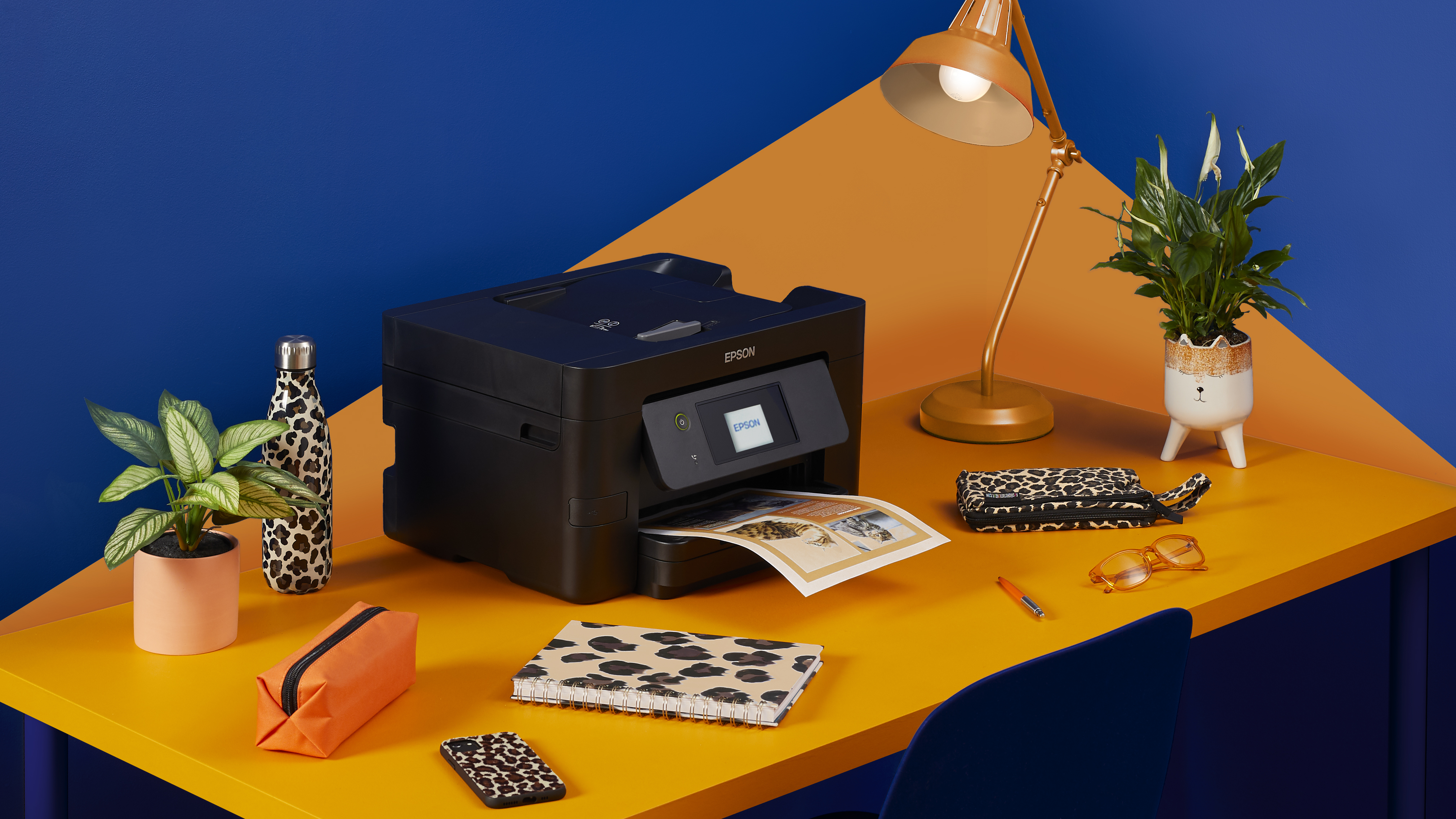Biurko z drukarką, lampą i rośliną. Przedmioty z nadrukiem w cętki, schemat kolorów pomarańczowy i niebieski.
