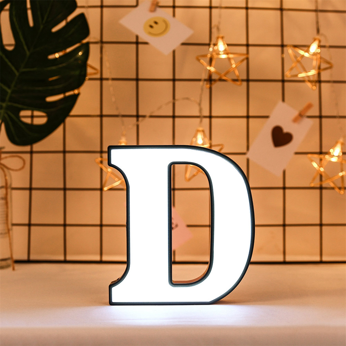 Ein beleuchteter weißer Buchstabe D vor einem Gitter, mit Lichterketten und dekorativen Gegenständen.