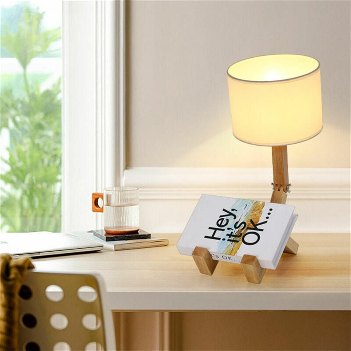 Eine Schreibtischlampe mit einem Buchhalter. Das Buch sagt: „Hey, es ist okay“. Es gibt auch einen Laptop.