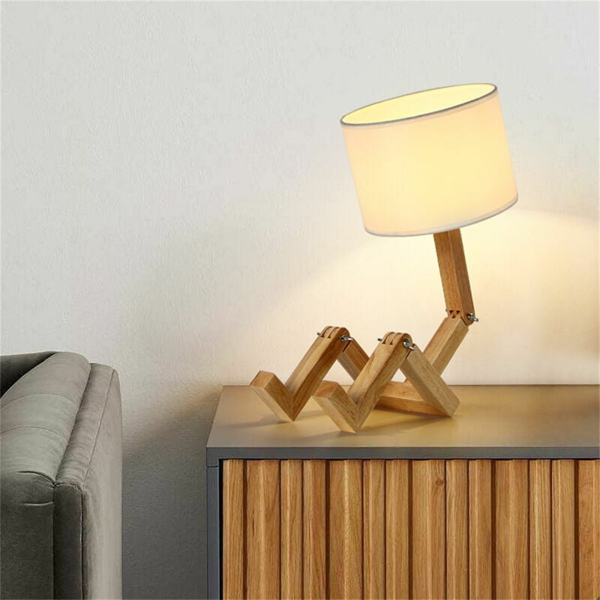 Holzlampe in Form einer Strichmännchenfigur auf einem Schrank. Die Lampe leuchtet.