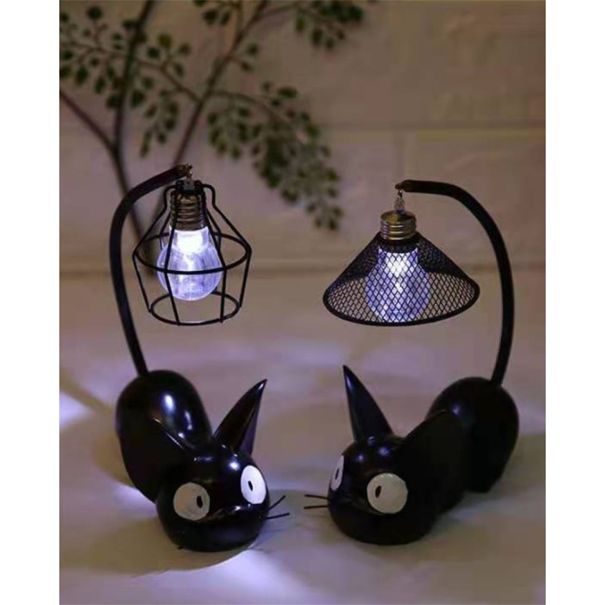 Zwei schwarze katzenförmige Lampen mit Lichtern im Inneren, auf neutralem Hintergrund.