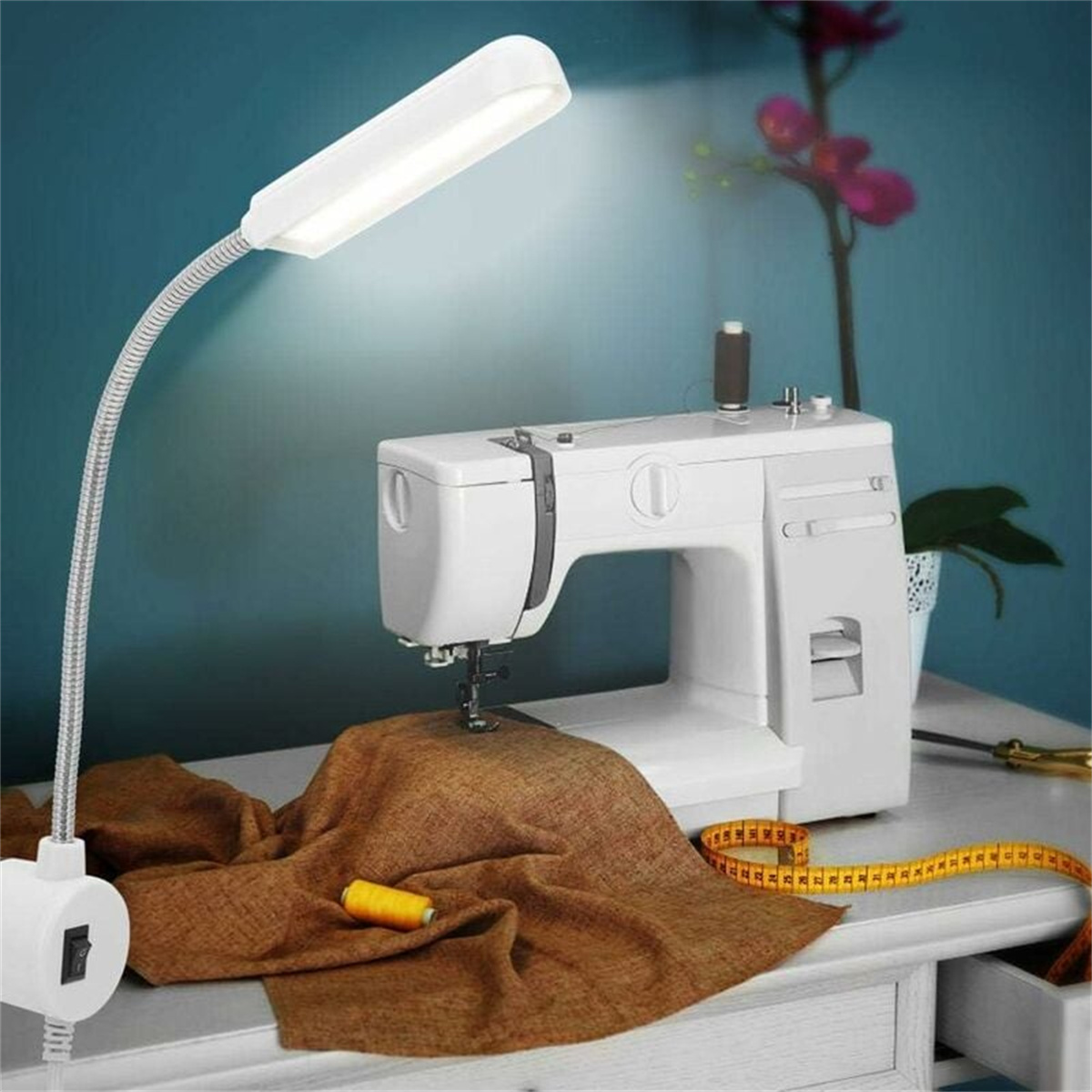Weiße Nähmaschine mit flexibler Lampe. Brauner Stoff unter der Nadel und ein Maßband.