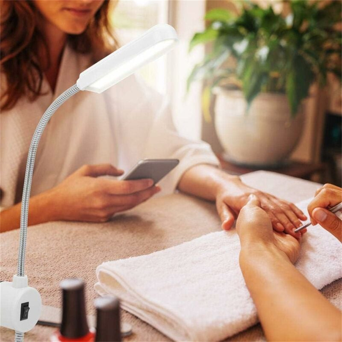 Person bekommt Maniküre. Lampe auf dem Tisch. Weißes Handtuch vorhanden.