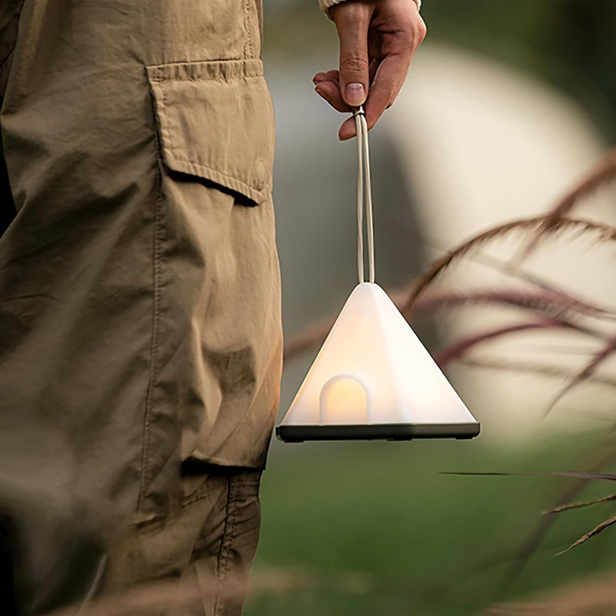 Ein Mann hält eine weiße, dreieckige Lampe mit Griff. Die Lampe ist beleuchtet.