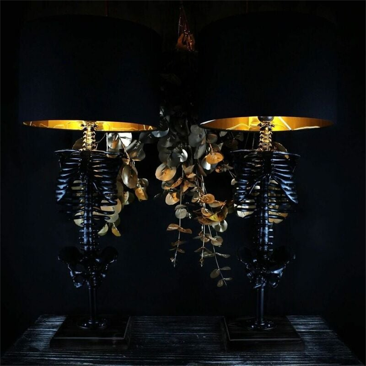Zwei Skelettlampen mit schwarzen Schirmen und goldenem Innenraum, symmetrisch angeordnet. Dunkler Hintergrund.