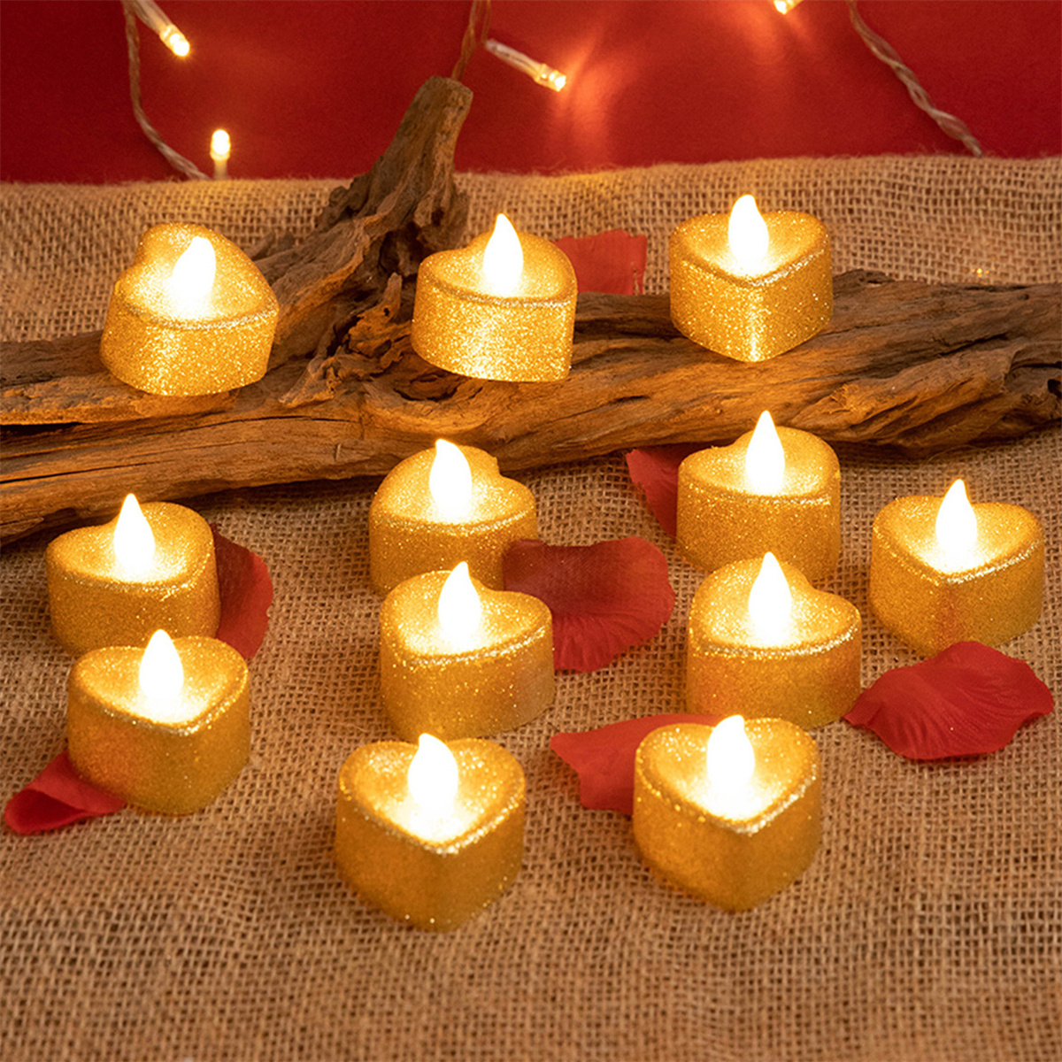 Herzförmige goldene Kerzen mit flackernden Flammen auf Jute und roten Blütenblättern. Ein Ast liegt oben.