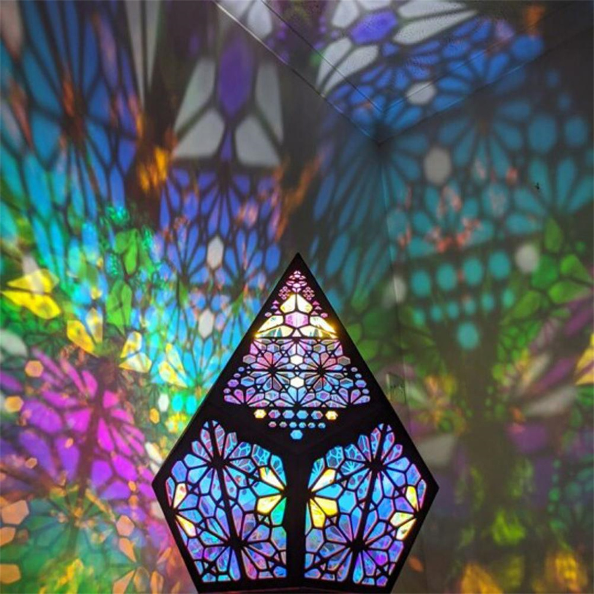 Eine geometrische Lampe, die farbenfrohe Muster auf eine Wand projiziert. Die Lampe hat eine dunkle Dreiecksform.