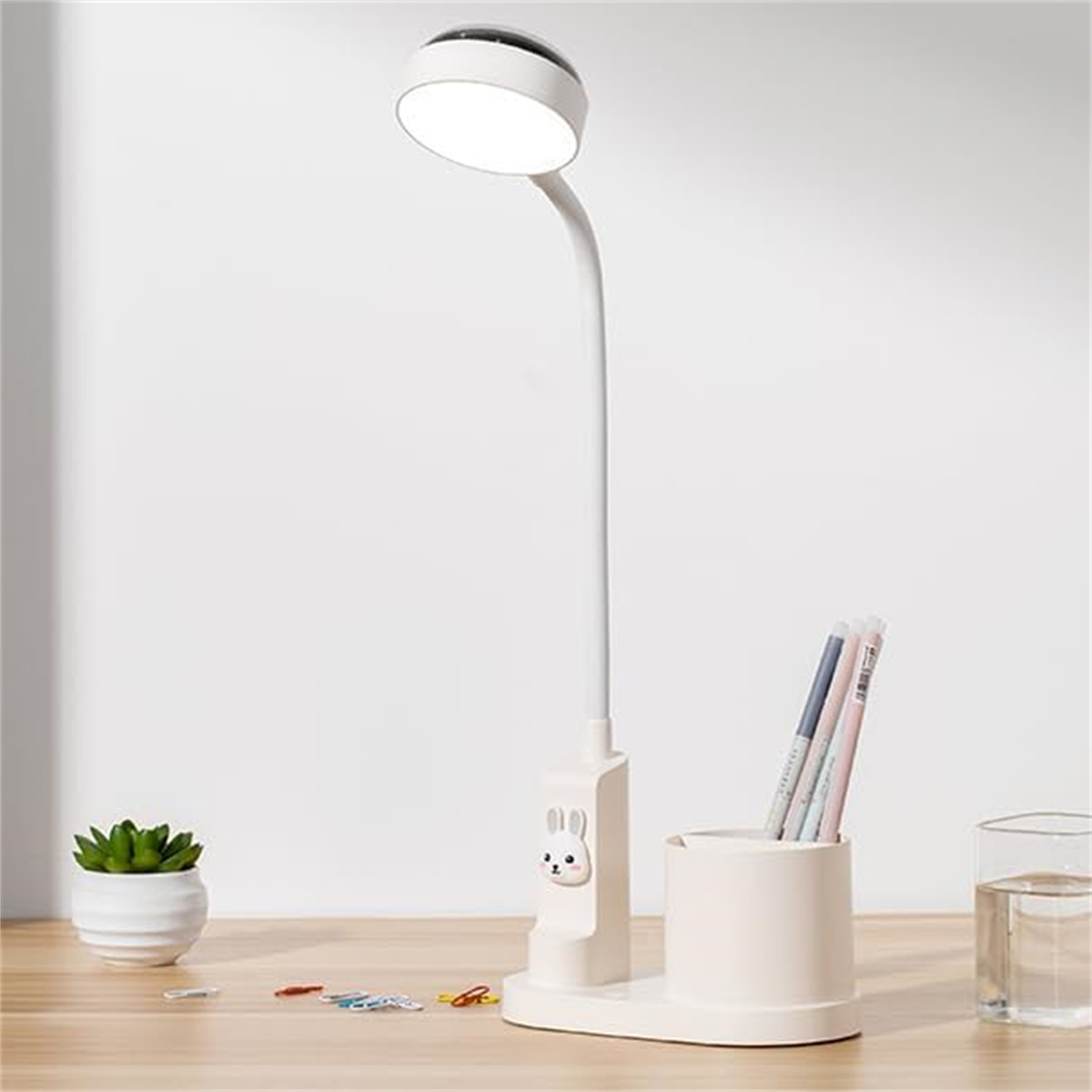 Weiße Lampe mit Stifthalter, Stiften und kleiner Pflanze. Holztisch.