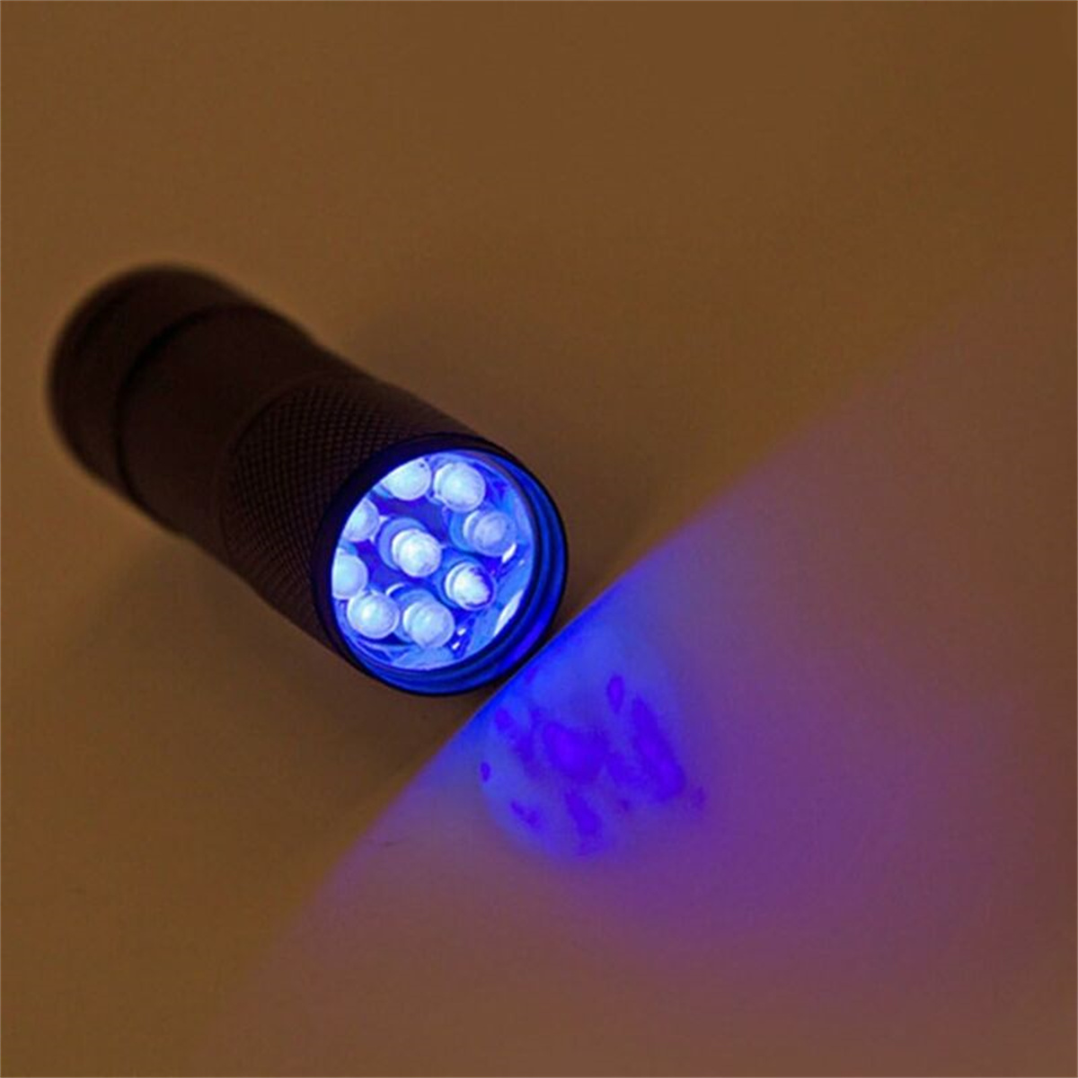 Schwarze Taschenlampe, die hellblaues Licht aussendet. Licht scheint auf Oberfläche. Dunkler Hintergrund.