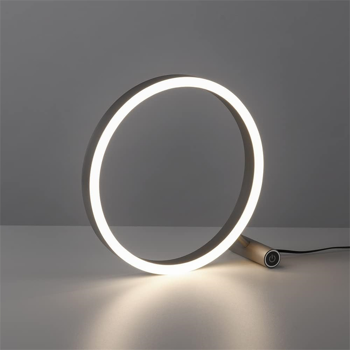 Eine ringförmige Lampe mit einem Ein-/Ausschalter am Sockel, die warmweißes Licht aussendet.