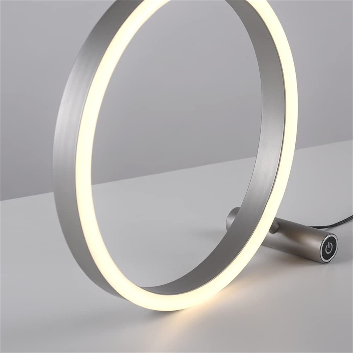 Eine moderne ringförmige Lampe. Das Licht ist an und die Lampe steht auf einer weißen Oberfläche.