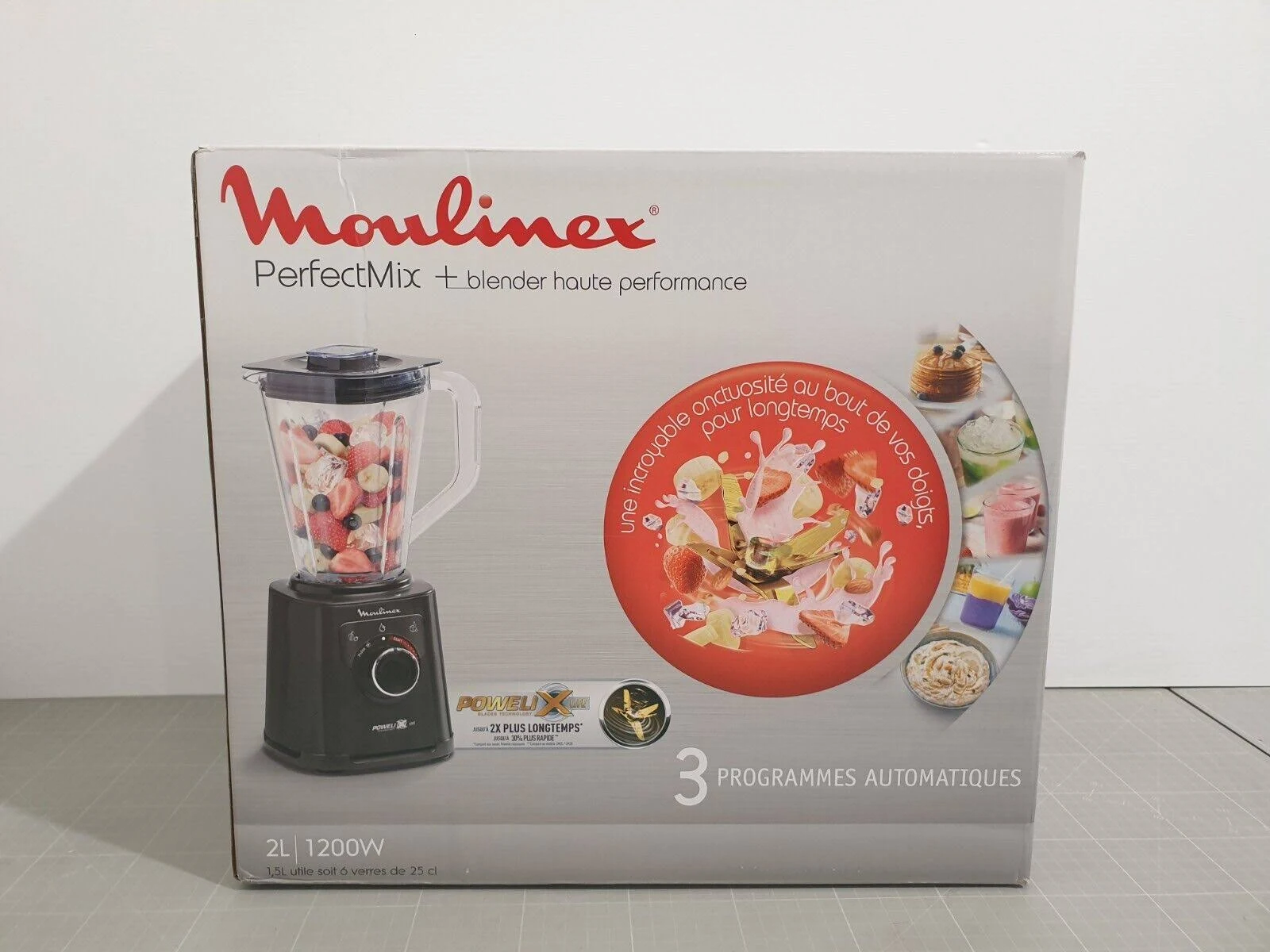 Se muestra una caja de la licuadora Moulinex. La licuadora es negra. La caja muestra frutas mezcladas.