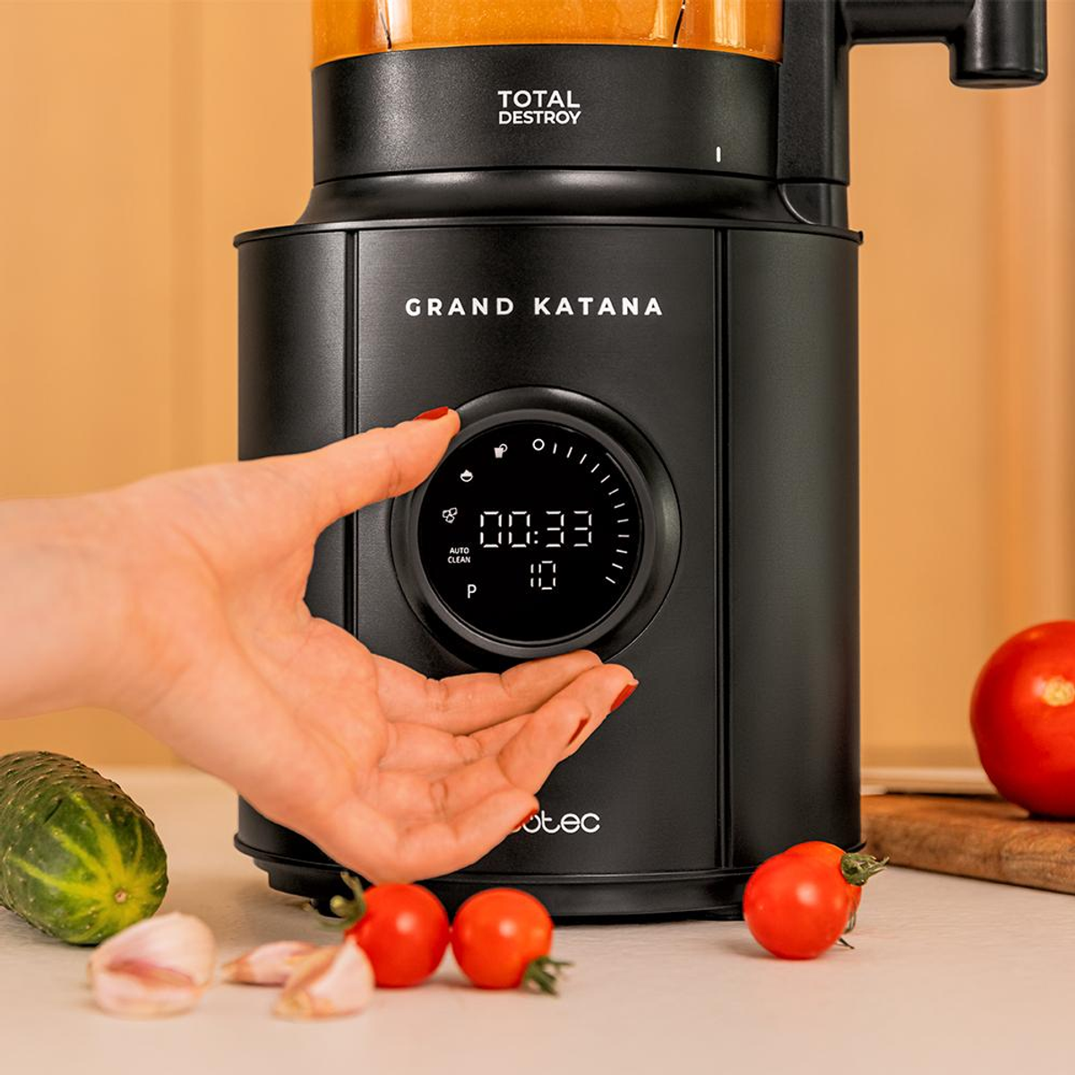 Ein Tisch mit Tomaten, Gurken, Knoblauch und einem schwarzen Total Destroy-Mixer. Hand in der Nähe.