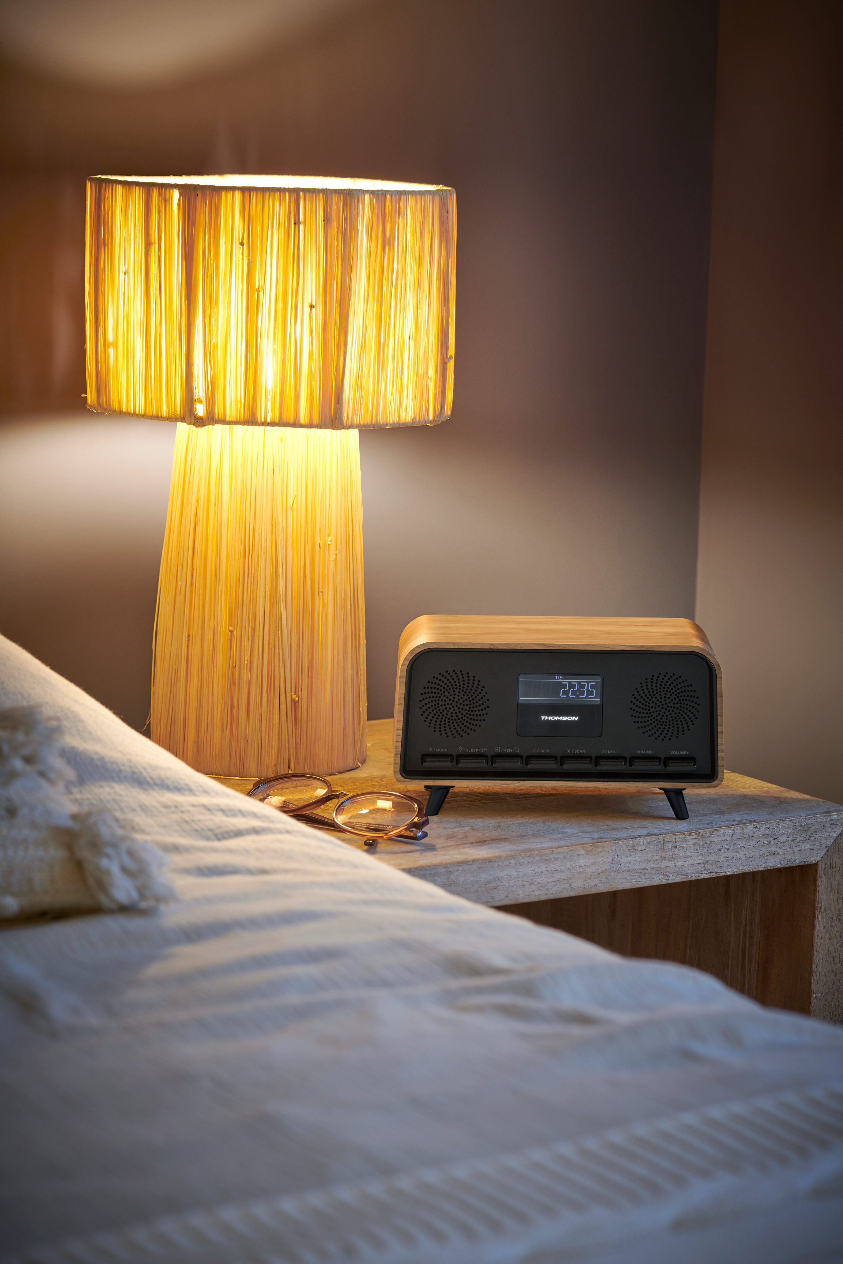 Scena przy łóżku z lampą i zegarem cyfrowym na drewnianym stoliku.