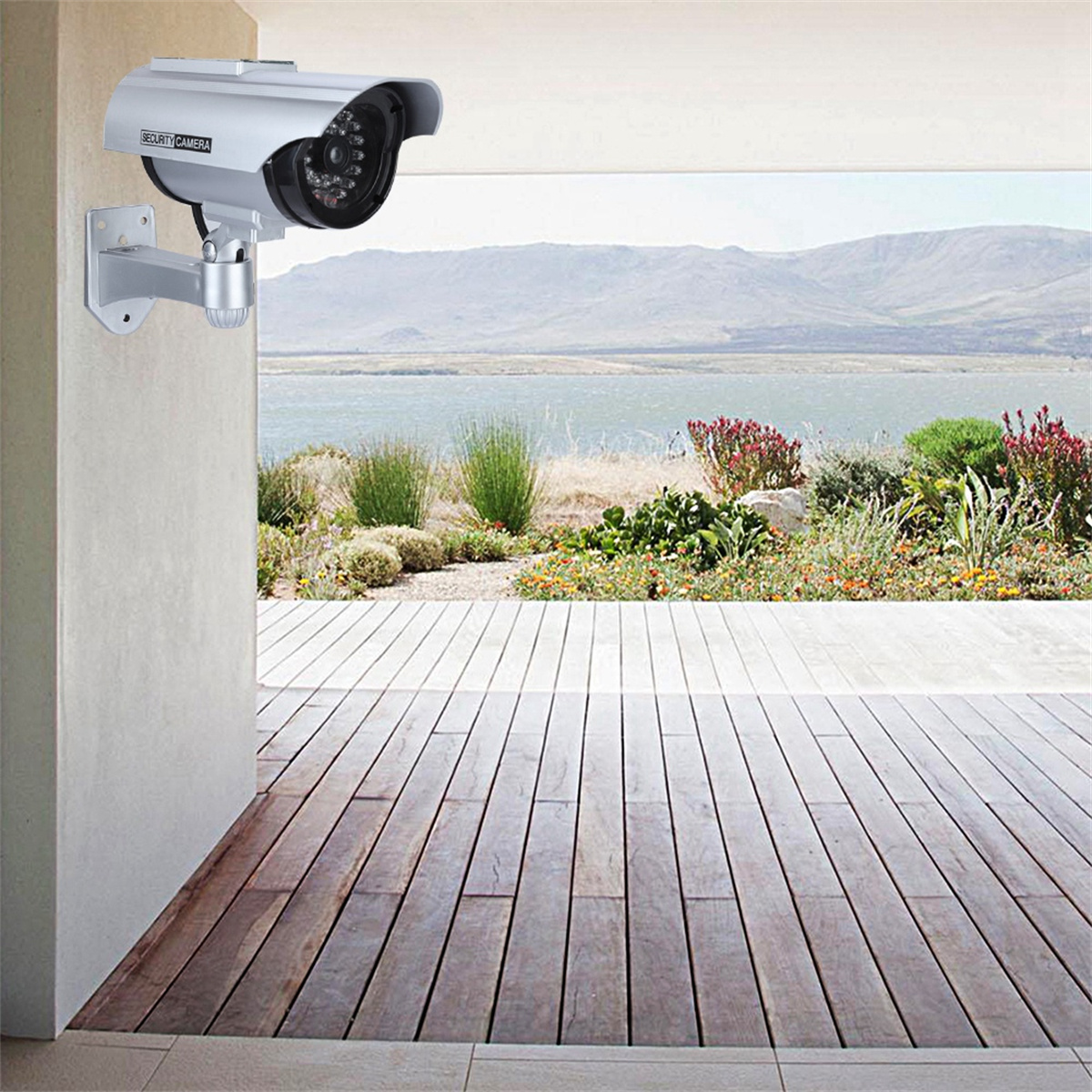 Silberne Überwachungskamera an einer Wand, mit Blick auf eine Holzterrasse und die Landschaft.