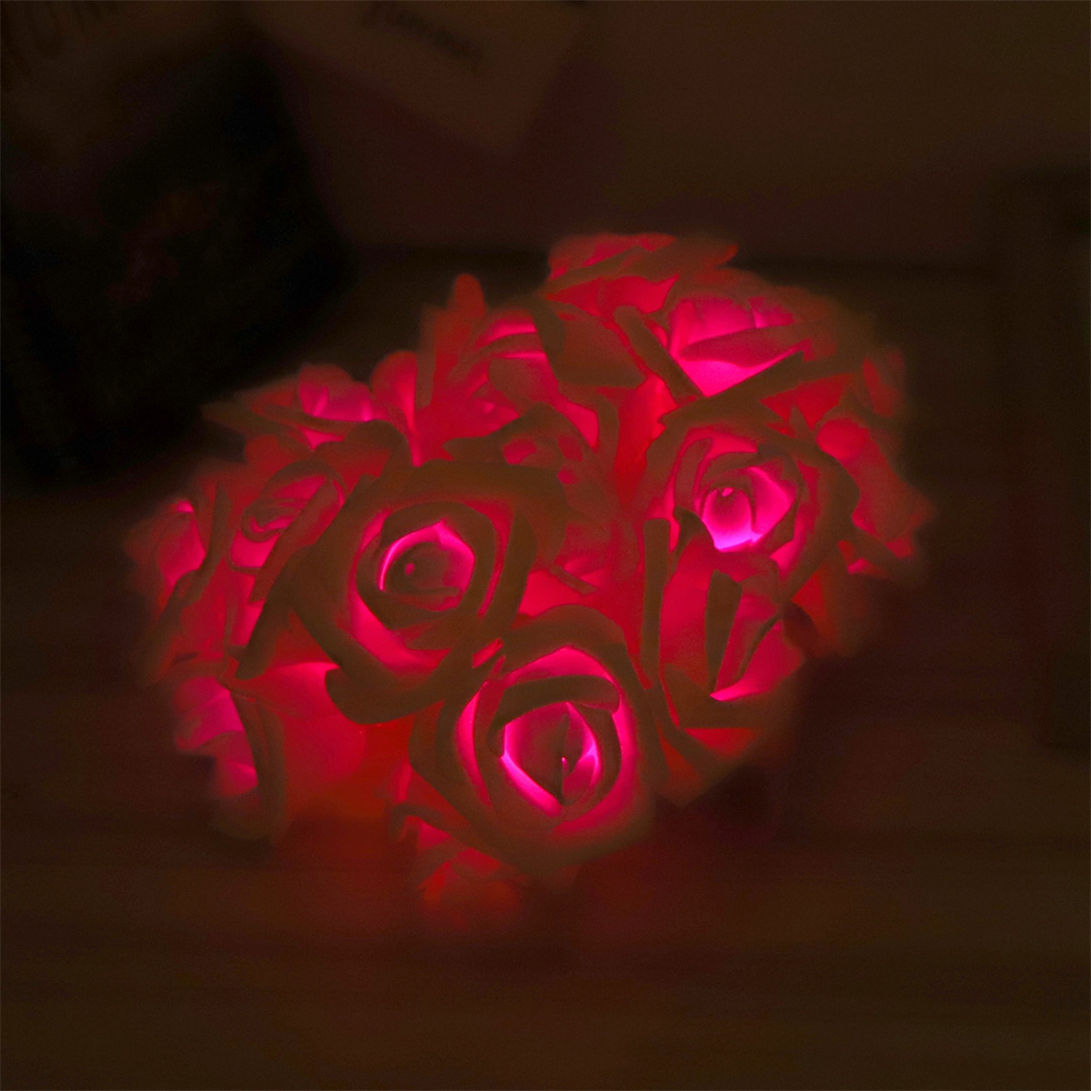 Nahaufnahme eines Straußes künstlicher Rosen, die in dunkler Umgebung rosa leuchten.