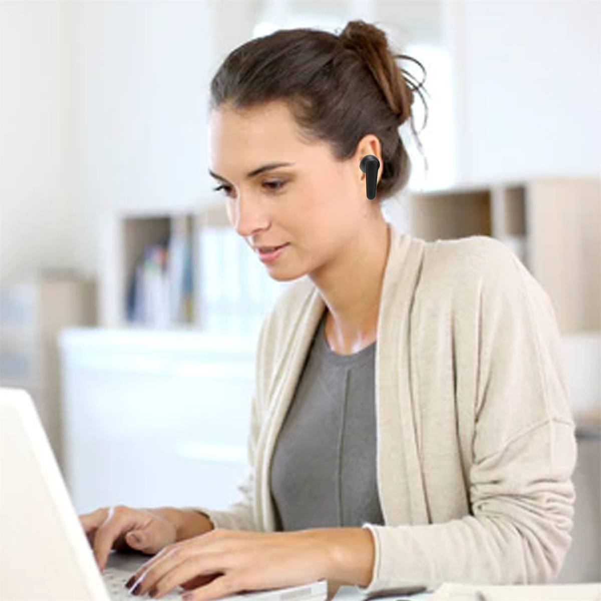 Frau mit Ohrhörer benutzt Laptop, konzentriert im Büro mit unscharfem Hintergrund.