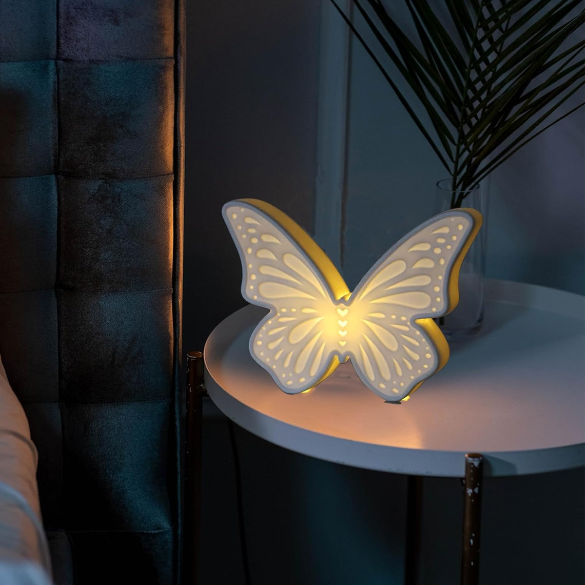 Schmetterlingsförmige Lampe auf einem weißen Tisch. Es gibt eine Vase mit Pflanzen. Dunkler Hintergrund.