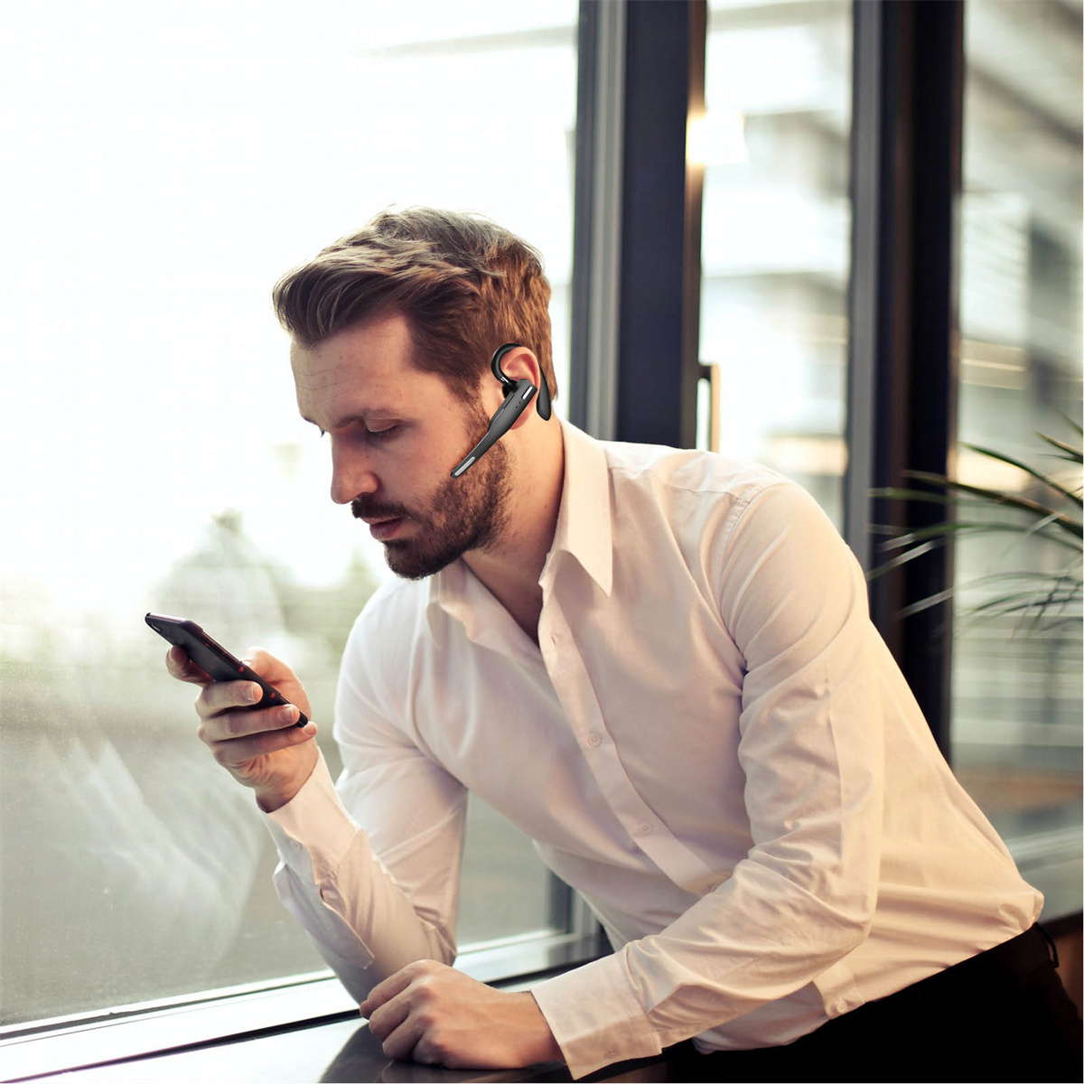 Mann mit Headset, der in der Nähe eines Fensters auf sein Telefon schaut.