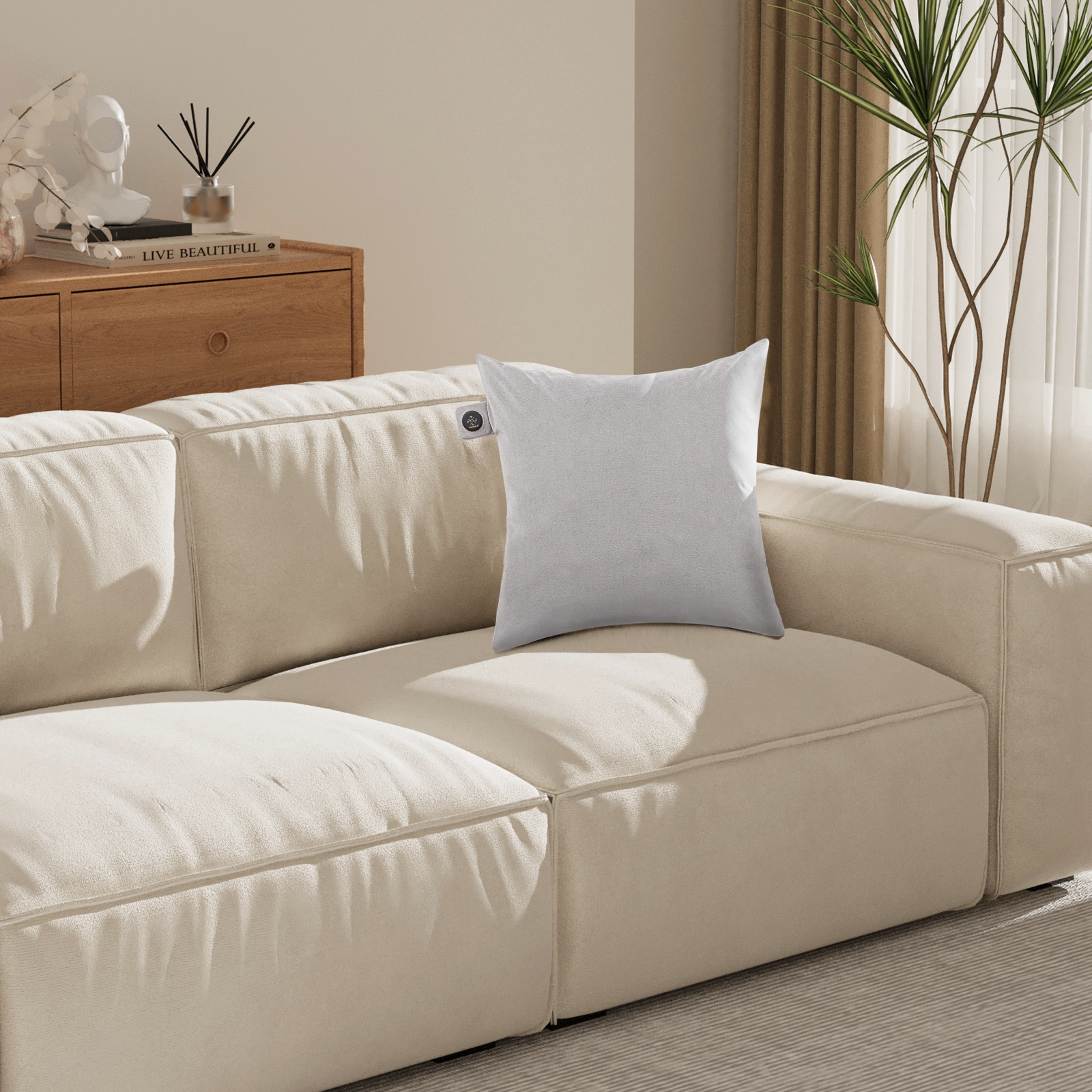 Ein graues Kissen auf einer cremefarbenen Couch. Die Couch befindet sich in einem hellen Raum.