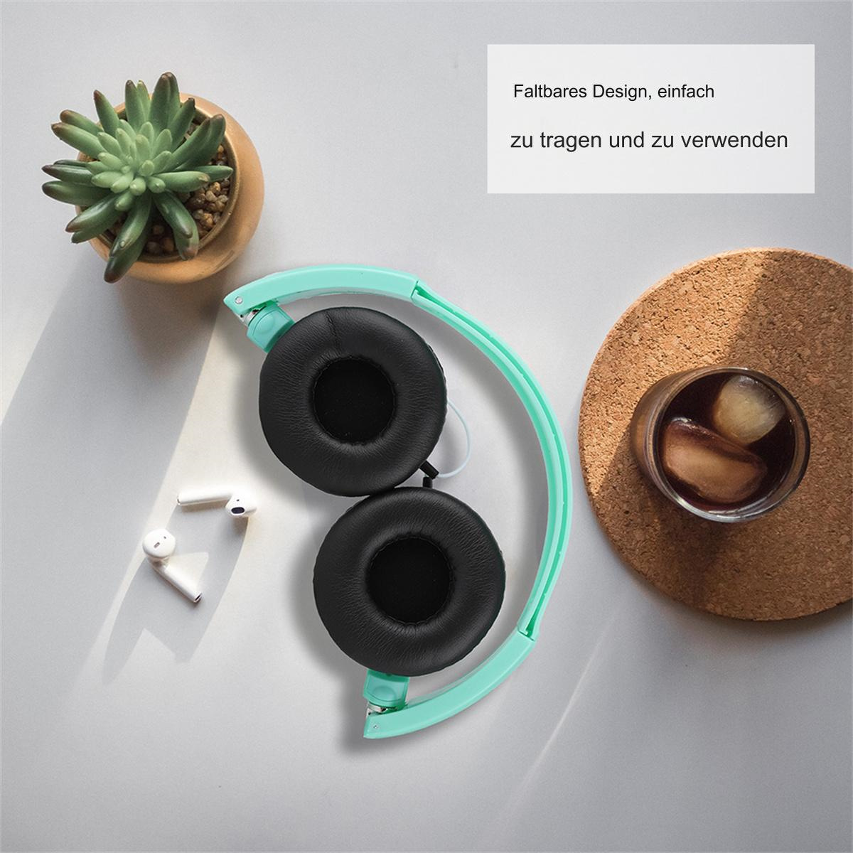 Faltbare Kopfhörer, kleine Pflanze und ein Glas mit Getränk auf einem Tisch.