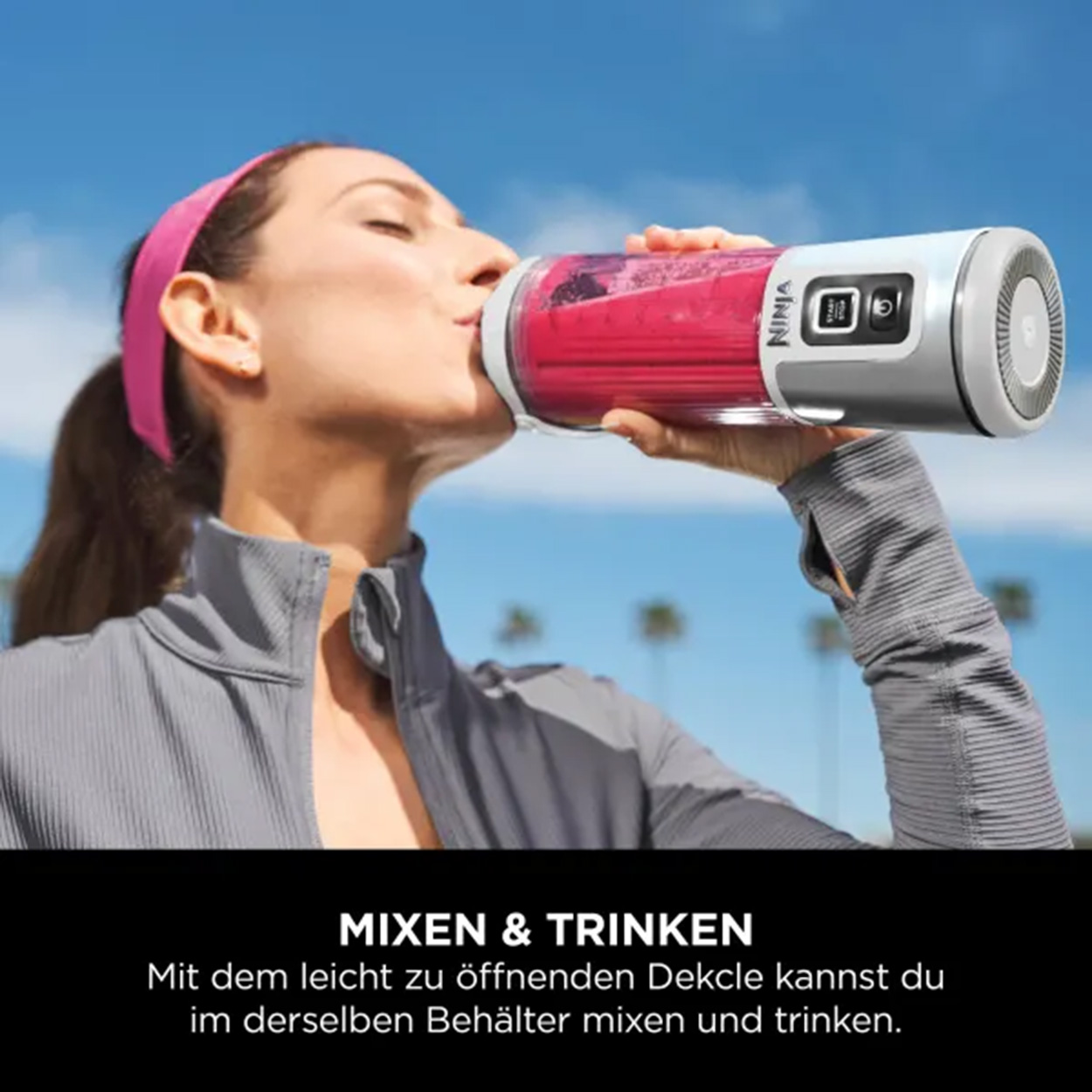 Eine Frau trinkt aus einer Ninja-Blenderflasche, blauer Himmel und Palmen im Hintergrund.