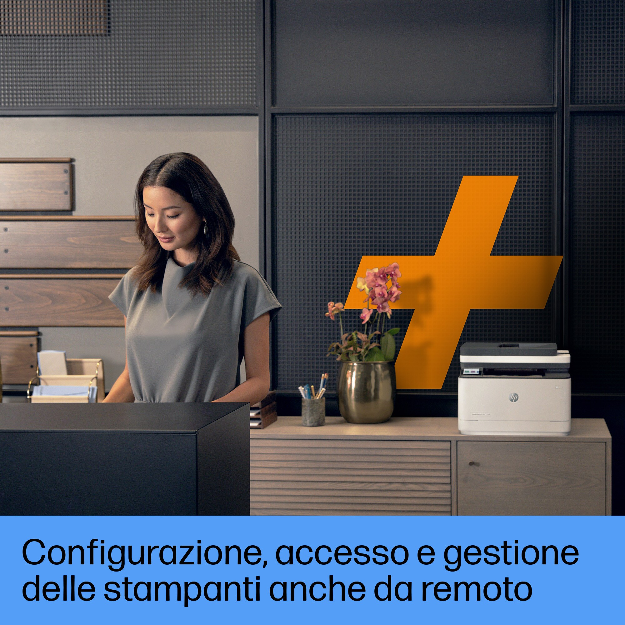 Una donna è in piedi a una scrivania con una stampante. L'ufficio ha un grande segno più sulla parete. Il testo è italiano.
