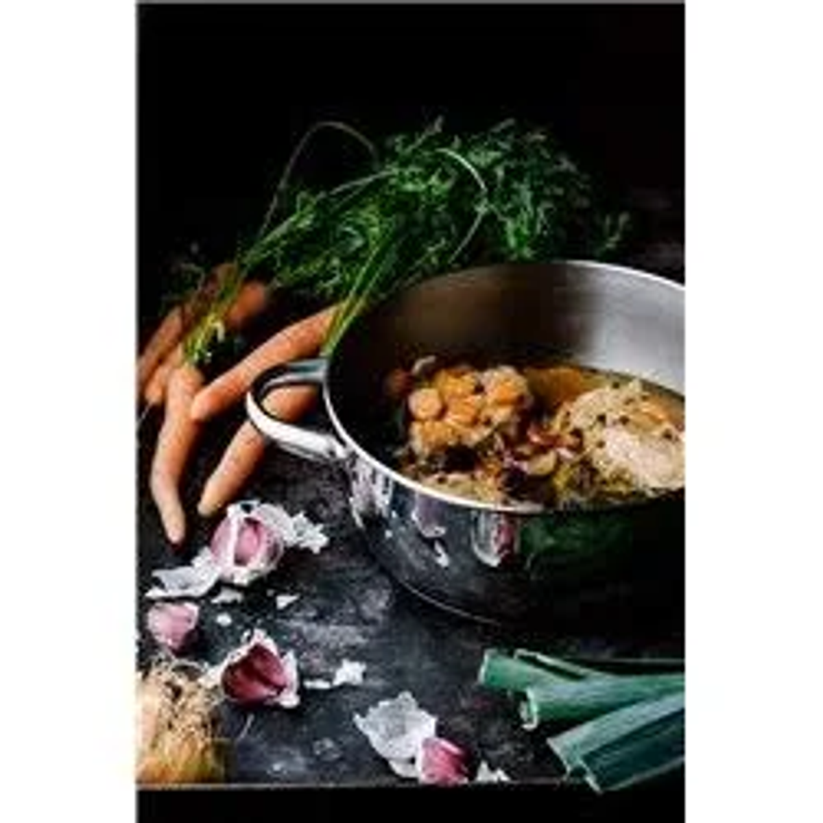 Una olla con comida cocinada, zanahorias, ajo y puerros se coloca sobre una superficie oscura y texturizada.