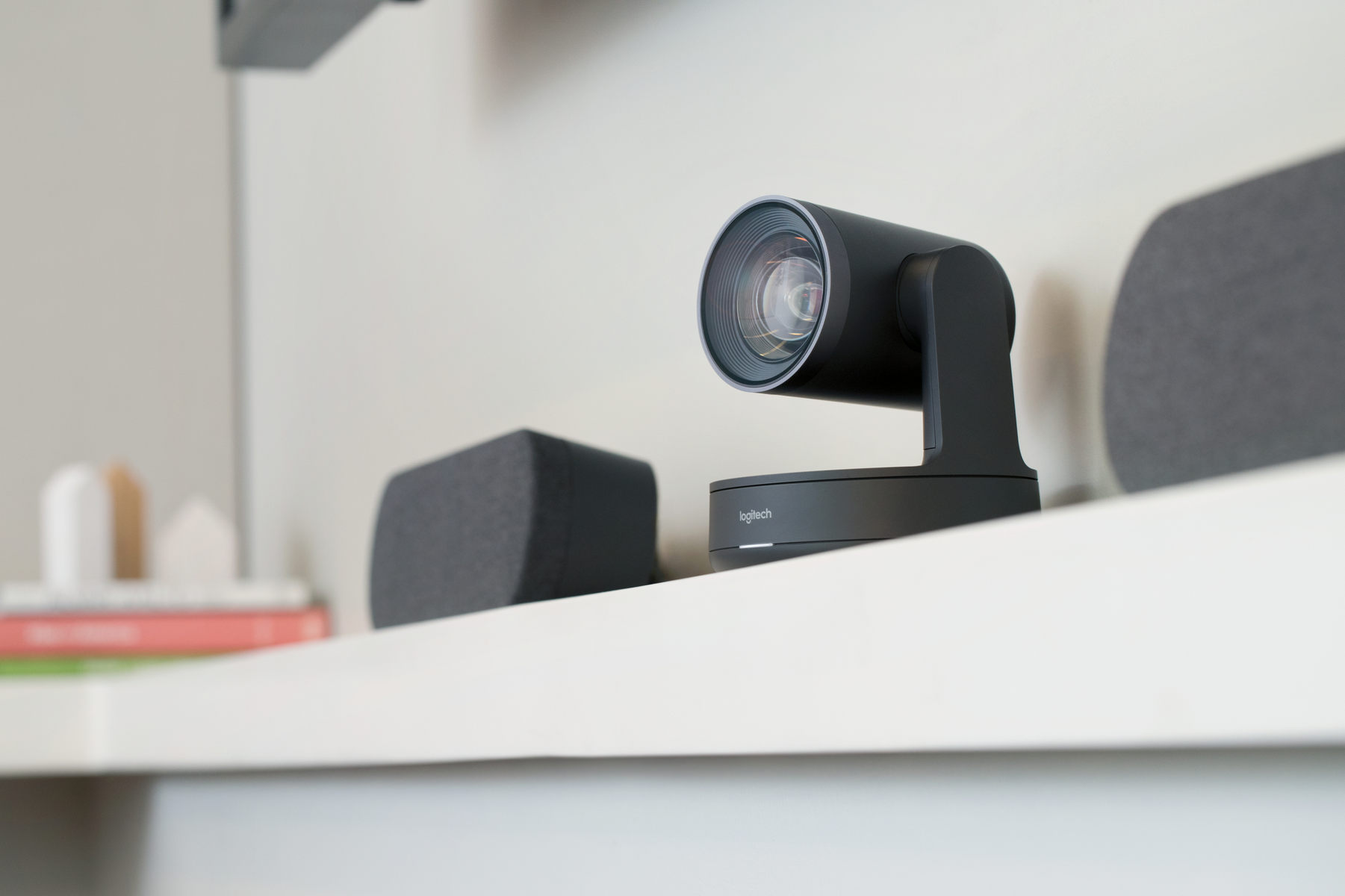 Schwarze Logitech Kamera auf einem weißen Regal montiert. Zwei Lautsprecher ebenfalls auf dem Regal.
