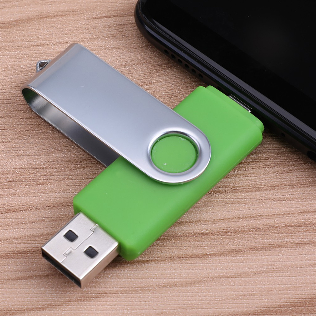 Grüner und silberner USB-Stick neben einem schwarzen Smartphone auf Holzoberfläche.