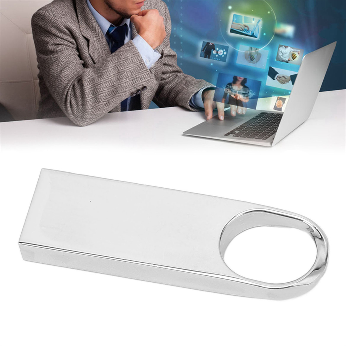 Ein silberner USB-Stick vor einem Laptop, ein Mann sitzt und benutzt einen Laptop.