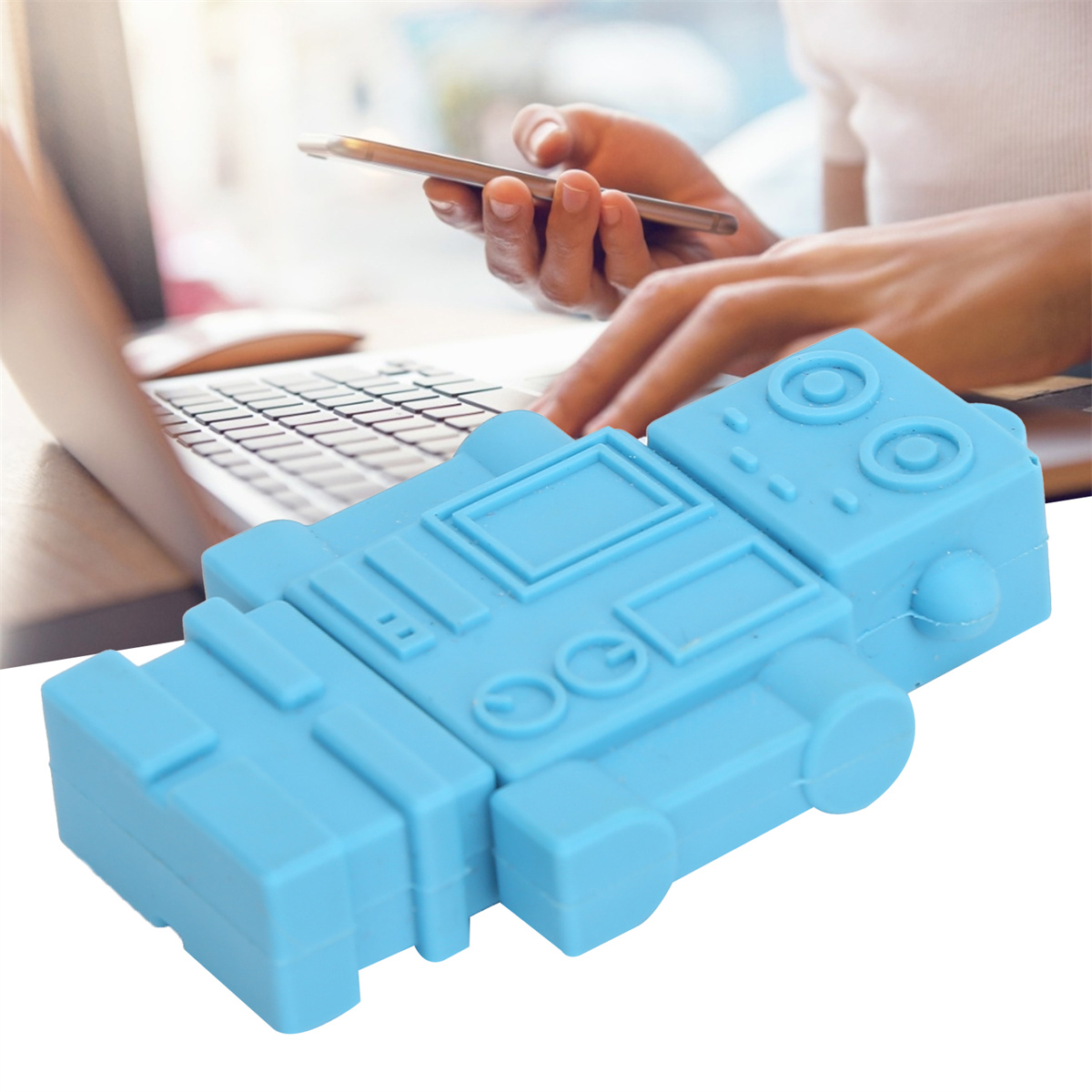 Ein blaues USB-Laufwerk in Roboterform auf einem Tisch, mit Laptop und Händen im Hintergrund.