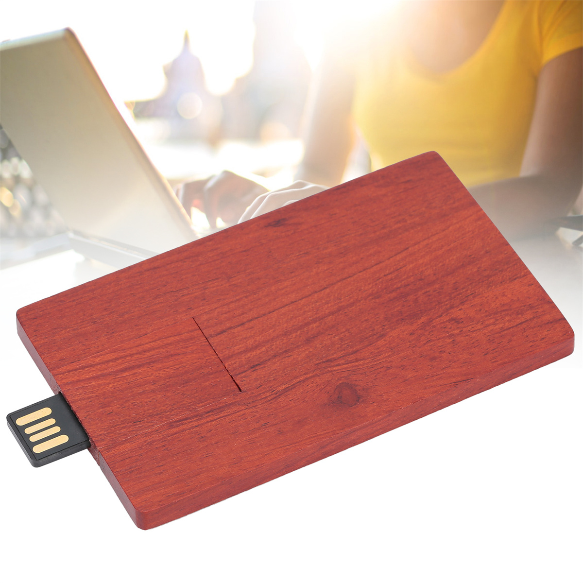 Ein USB-Stick aus Holz liegt auf einem Schreibtisch, im Hintergrund ist ein Laptop zu sehen.
