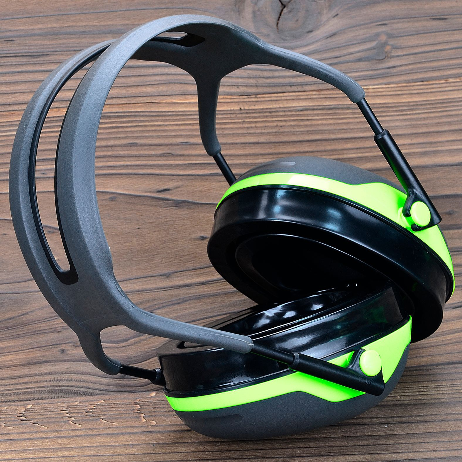 Ochrona słuchu z redukcją szumów. Na drewnianej powierzchni czarne i zielone nauszniki.