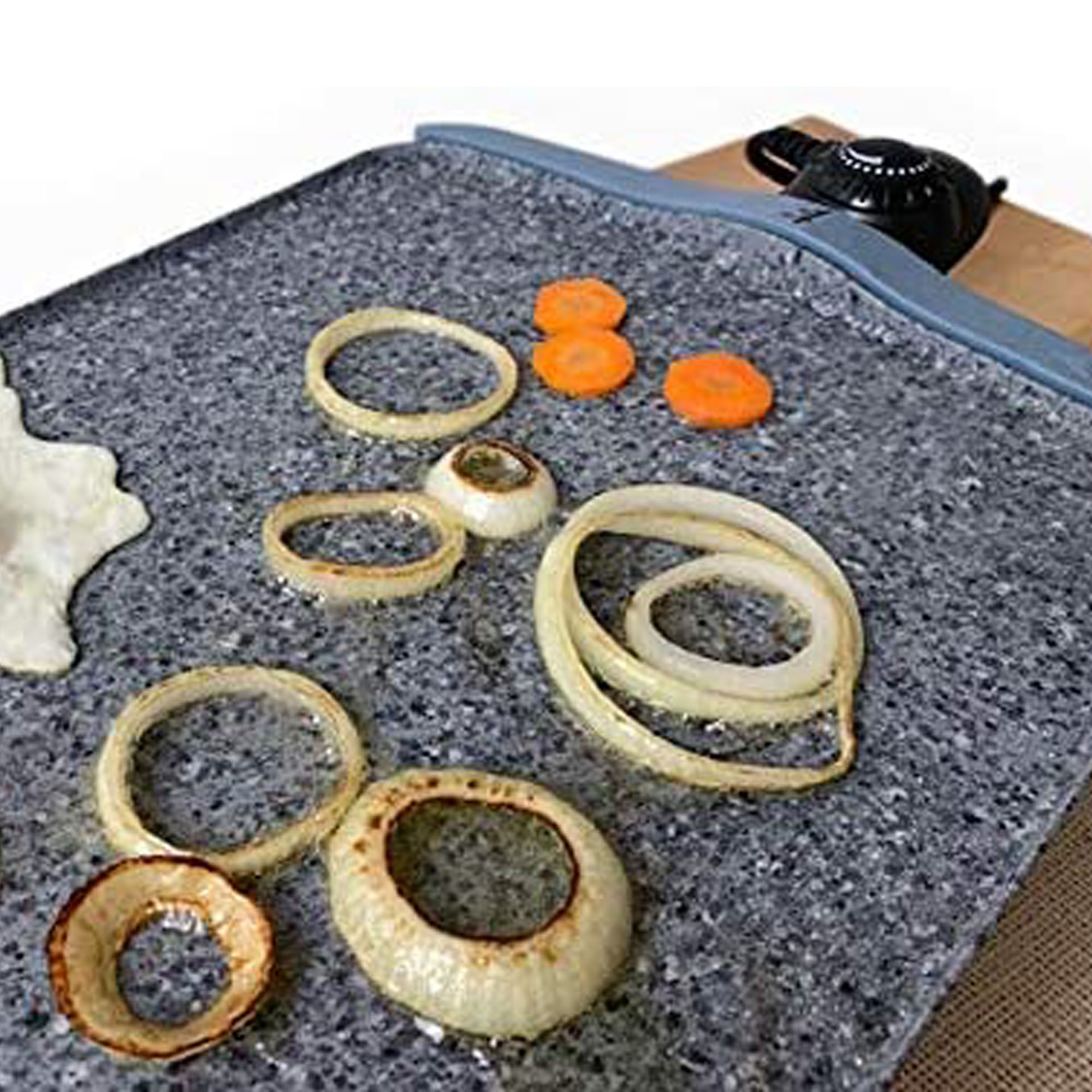 Rodajas de cebolla y zanahoria dispuestas sobre una superficie de piedra, con un pequeño recipiente negro al fondo.