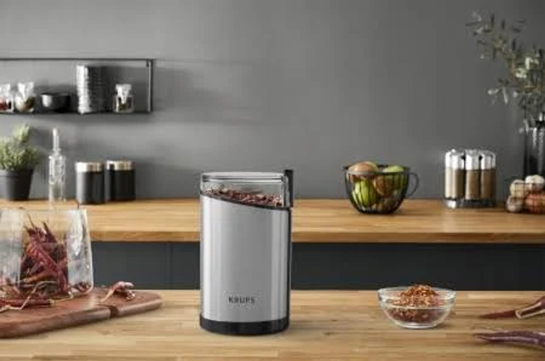 Młynek do kawy Krups z ziarnami kawy w środku, na drewnianym blacie w kuchni.