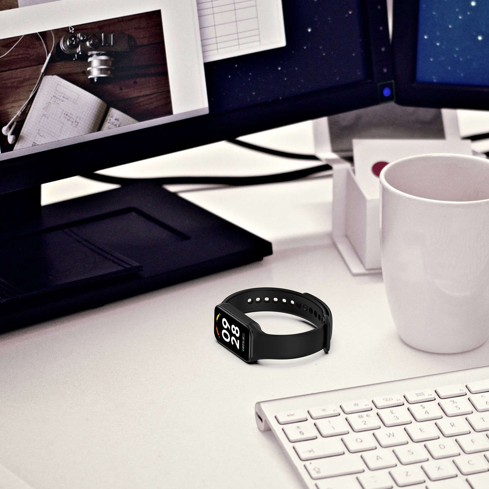 Czarny smartwatch na białym biurku obok klawiatury i kubka.