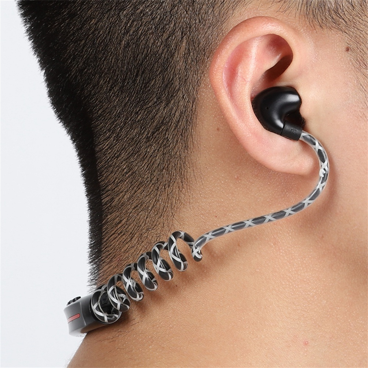 Das Ohr eines Mannes mit einem schwarzen Ohrhörer und einem gewendelten, grauen Kabel.