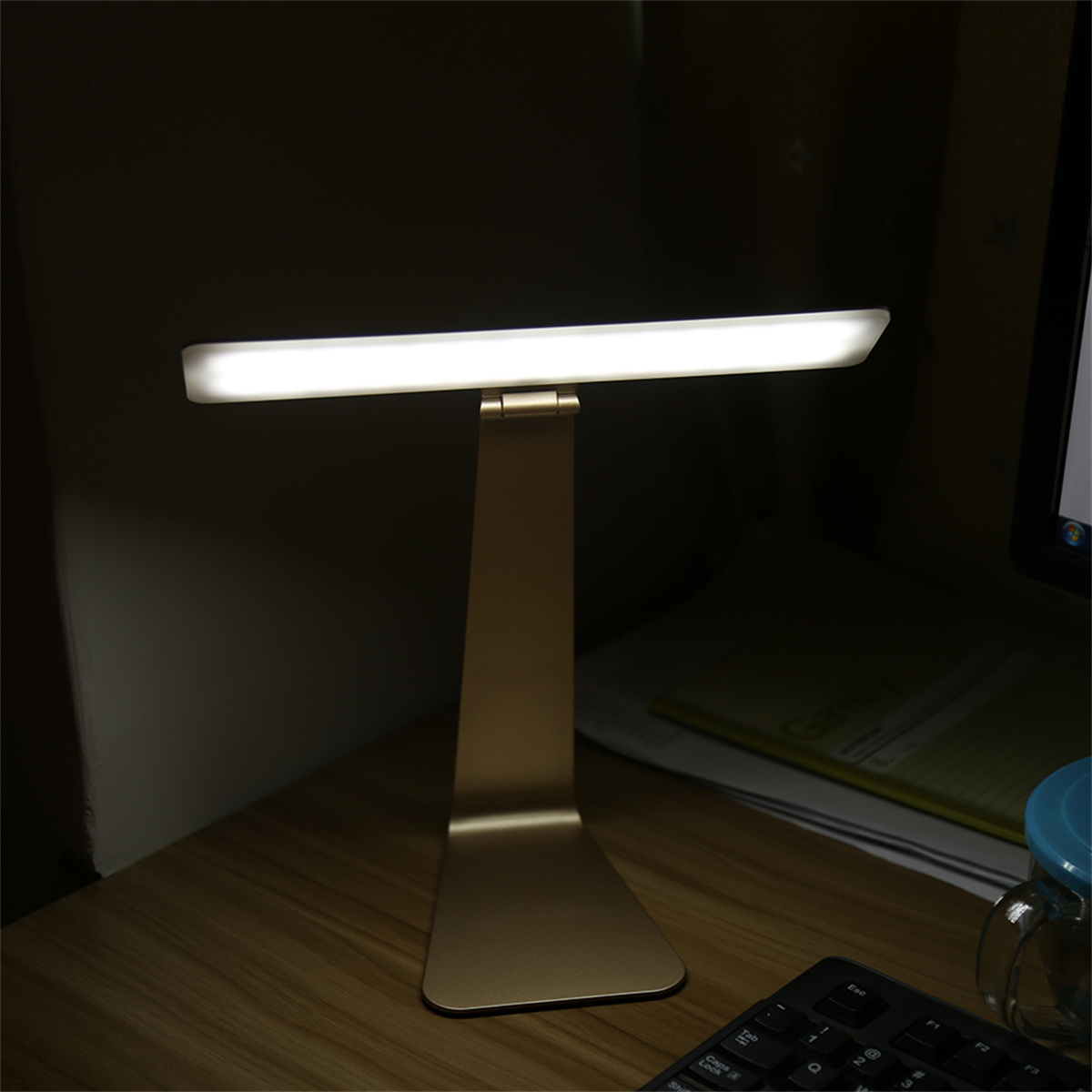 Schreibtischlampe, goldener Sockel und hellweißes Licht. Sie ist eingeschaltet.