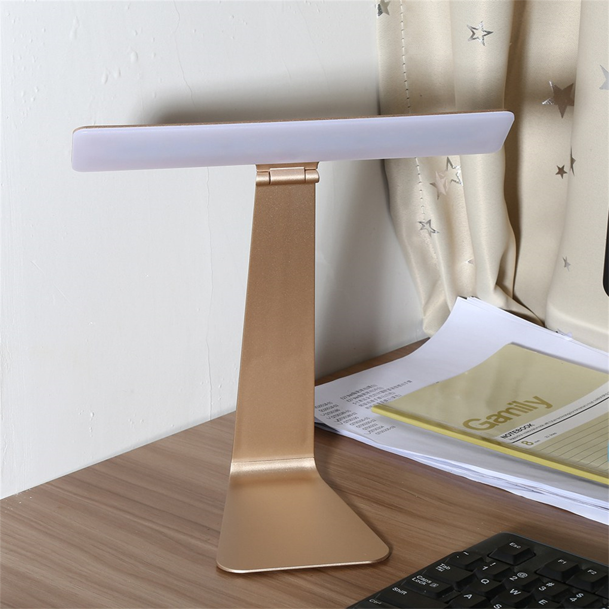 Goldene Schreibtischlampe, rechteckiges Licht, auf einem Schreibtisch mit Papieren und Tastatur. Das Licht ist an.