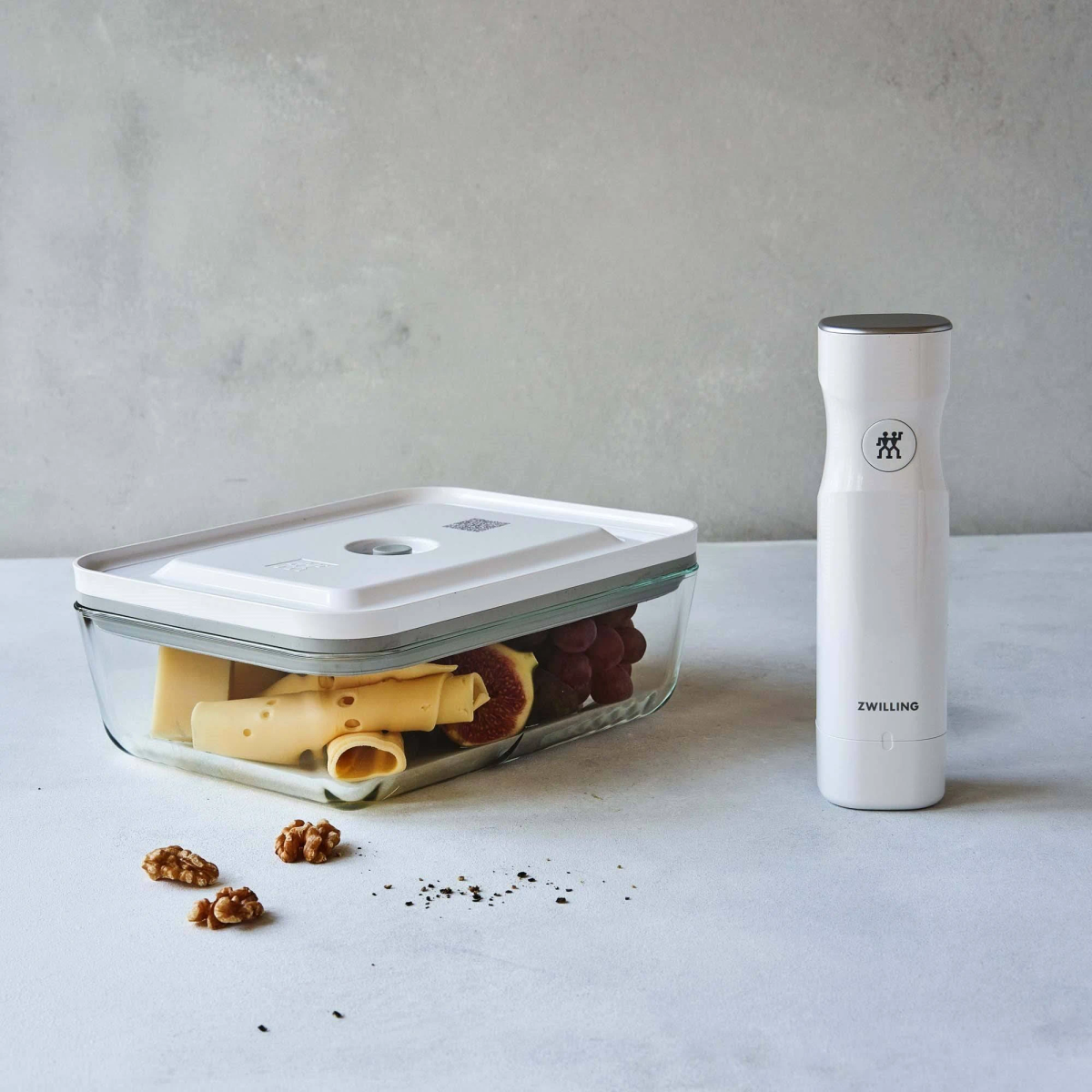 Szklany pojemnik z żywnością i biała zgrzewarka próżniowa na białej powierzchni.