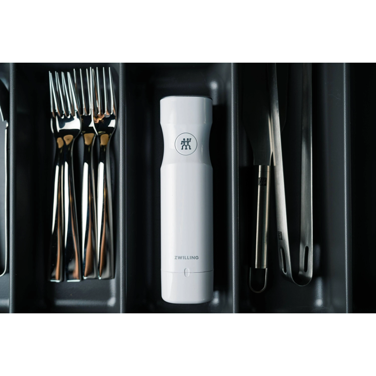 Srebrne widelce, biała solniczka Zwilling i szczypce w szufladzie.