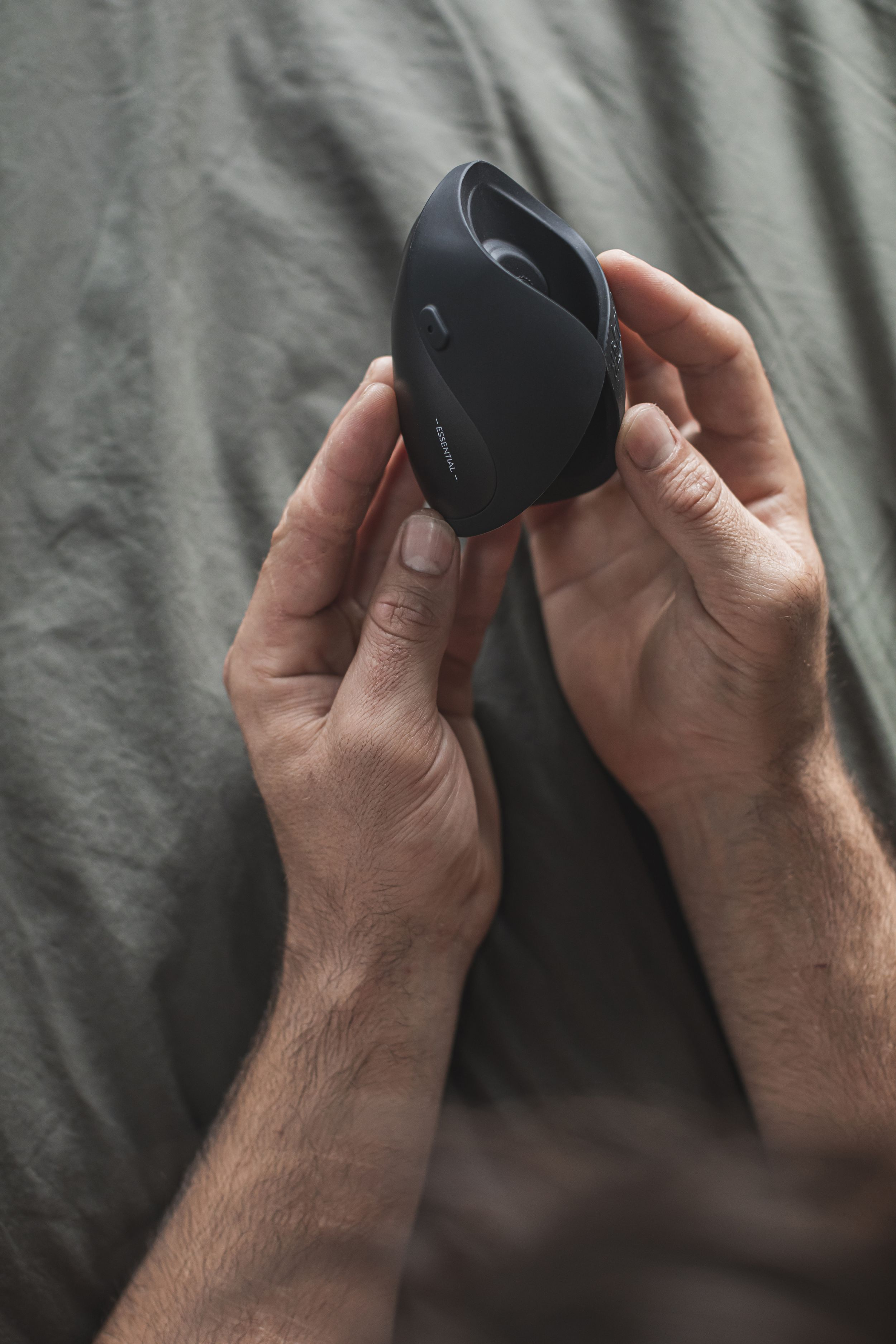 Dłonie trzymające czarne, zaokrąglone urządzenie. Urządzenie ma napis "ESSENTIAL".